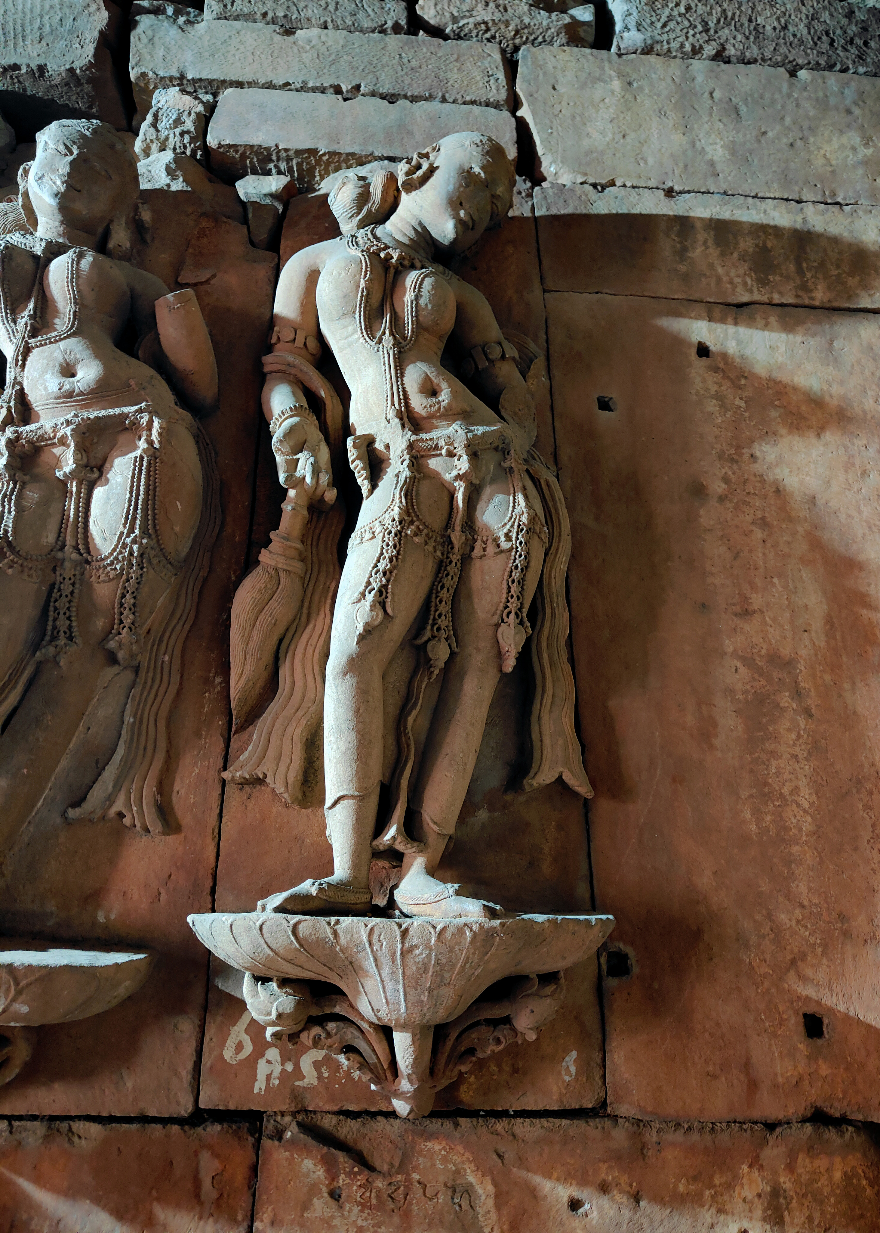 Image 4: There are beautiful nayika sculptures on the wall inside the temple sanctum. The 10th-century Kutila script inscribes epithets on most of them. The two-armed damsel carries a chamara fly whisk.