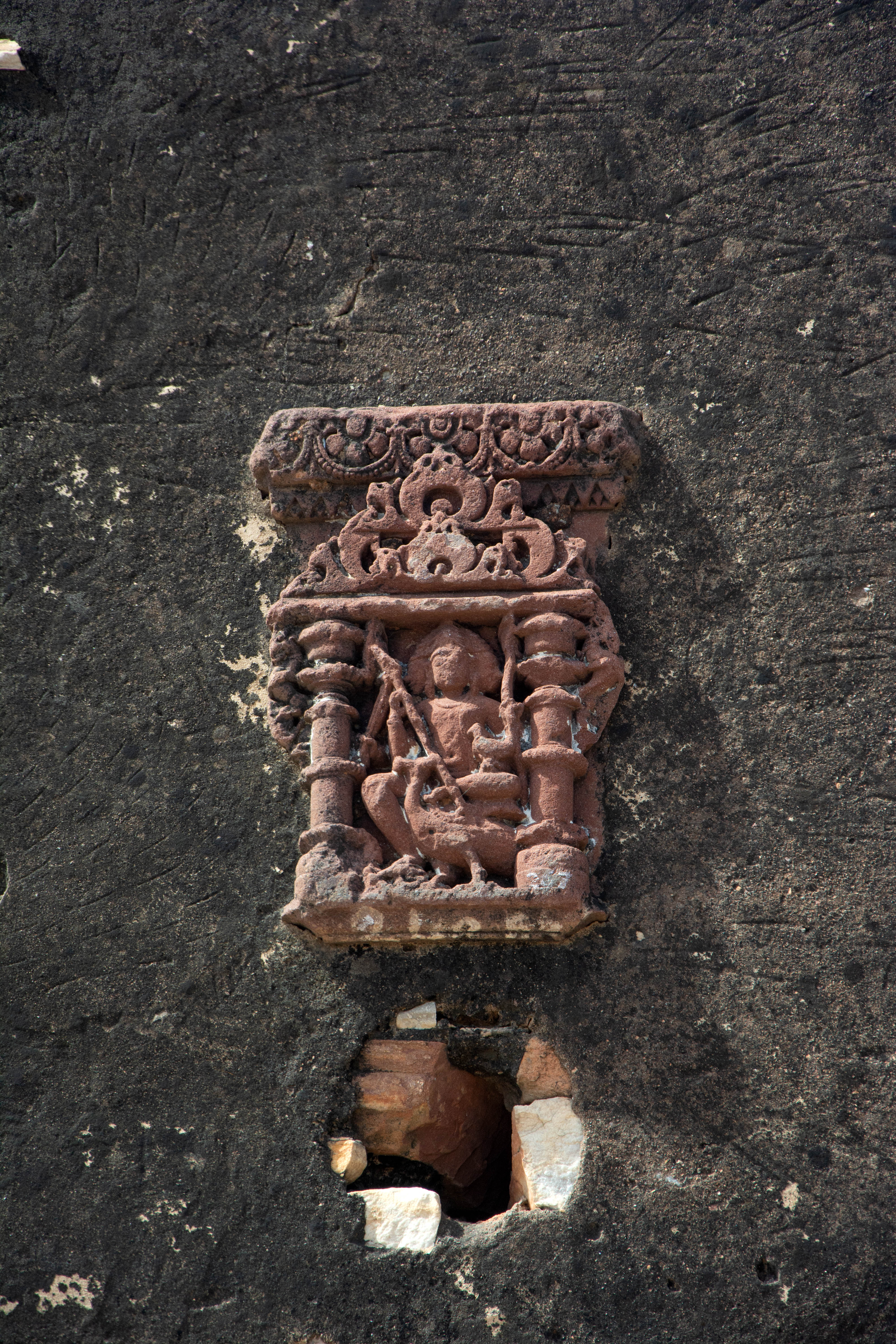 Kartikeya, with three visible faces, rests on his vahana, a peacock, which is placed on the devakostha (wall niches).