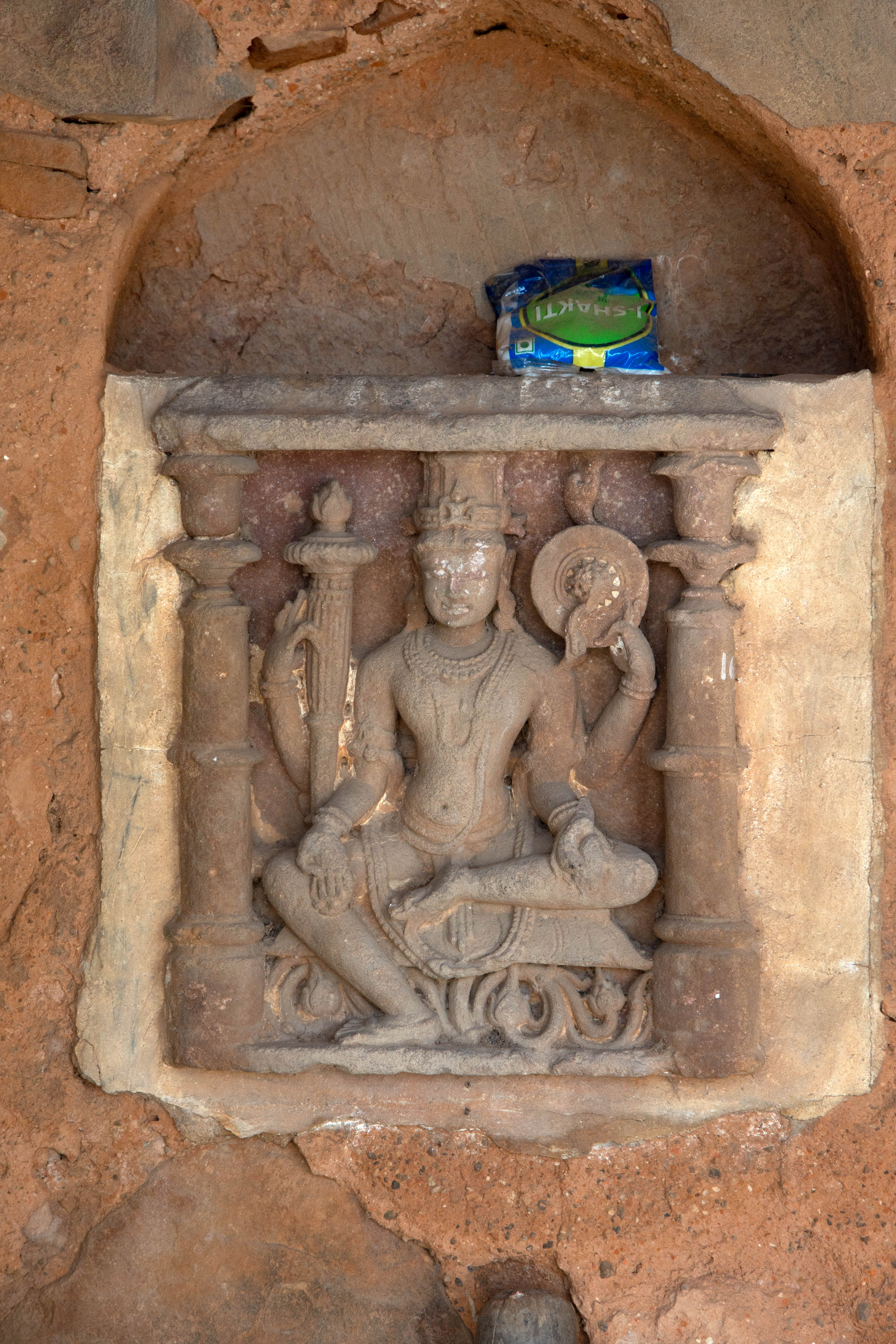 The depiction shows a four-armed Vishnu sitting in the lalitasana posture. He carries a mace and a chakra in his upper right and left hands, respectively, while the lower right and left hands hold a mala and possibly a citron, respectively.