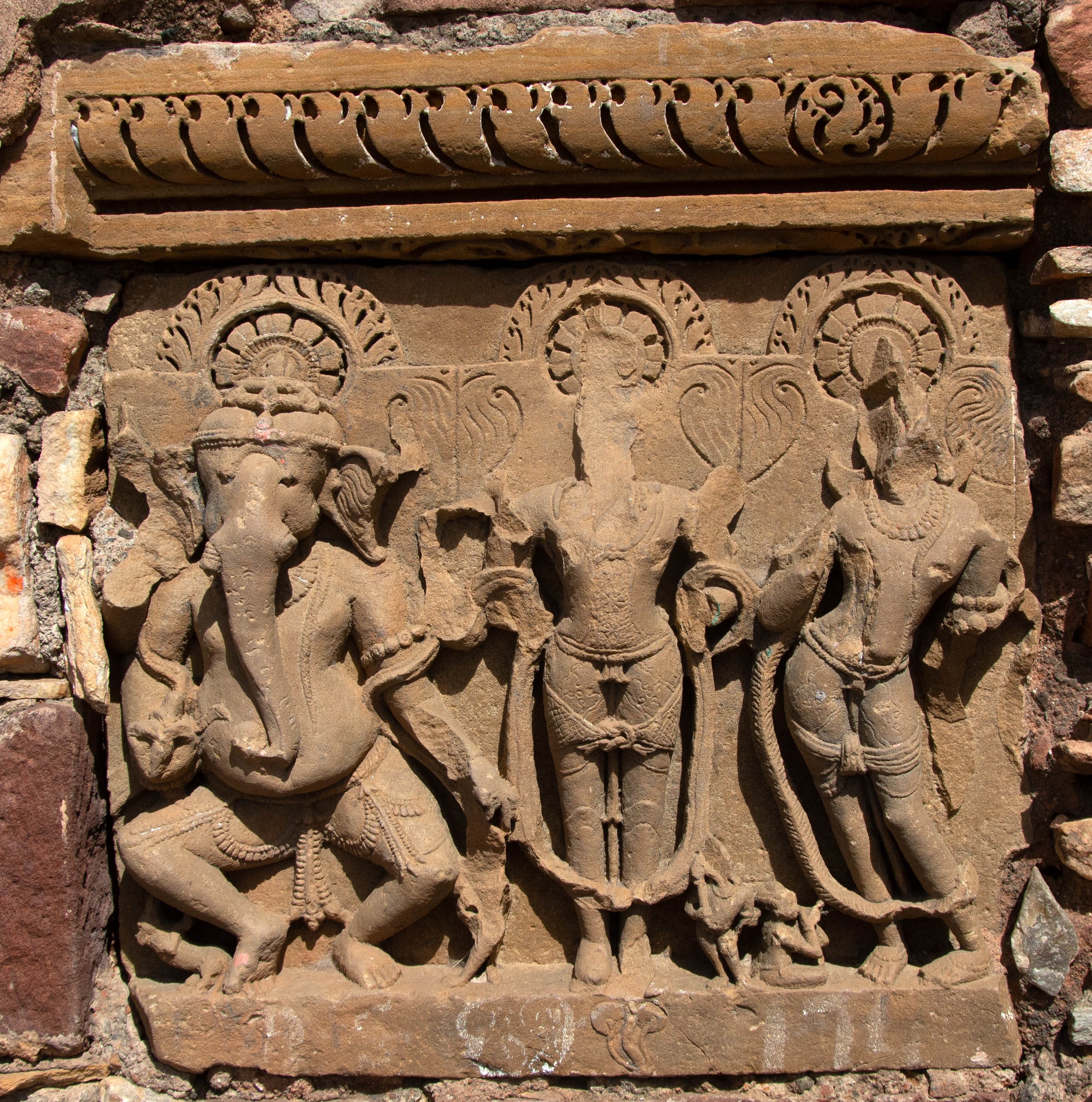 The trio of Ganesha, Surya, and Chandra is one of the several loose sculptures that were affixed to the later structures at the site. The three figures may have once been part of a larger panel depicting the nine heavenly bodies, or the navagraha. While the dancing Ganesha is four-armed, the images of Surya and Chandra have only two arms, broken in both cases.