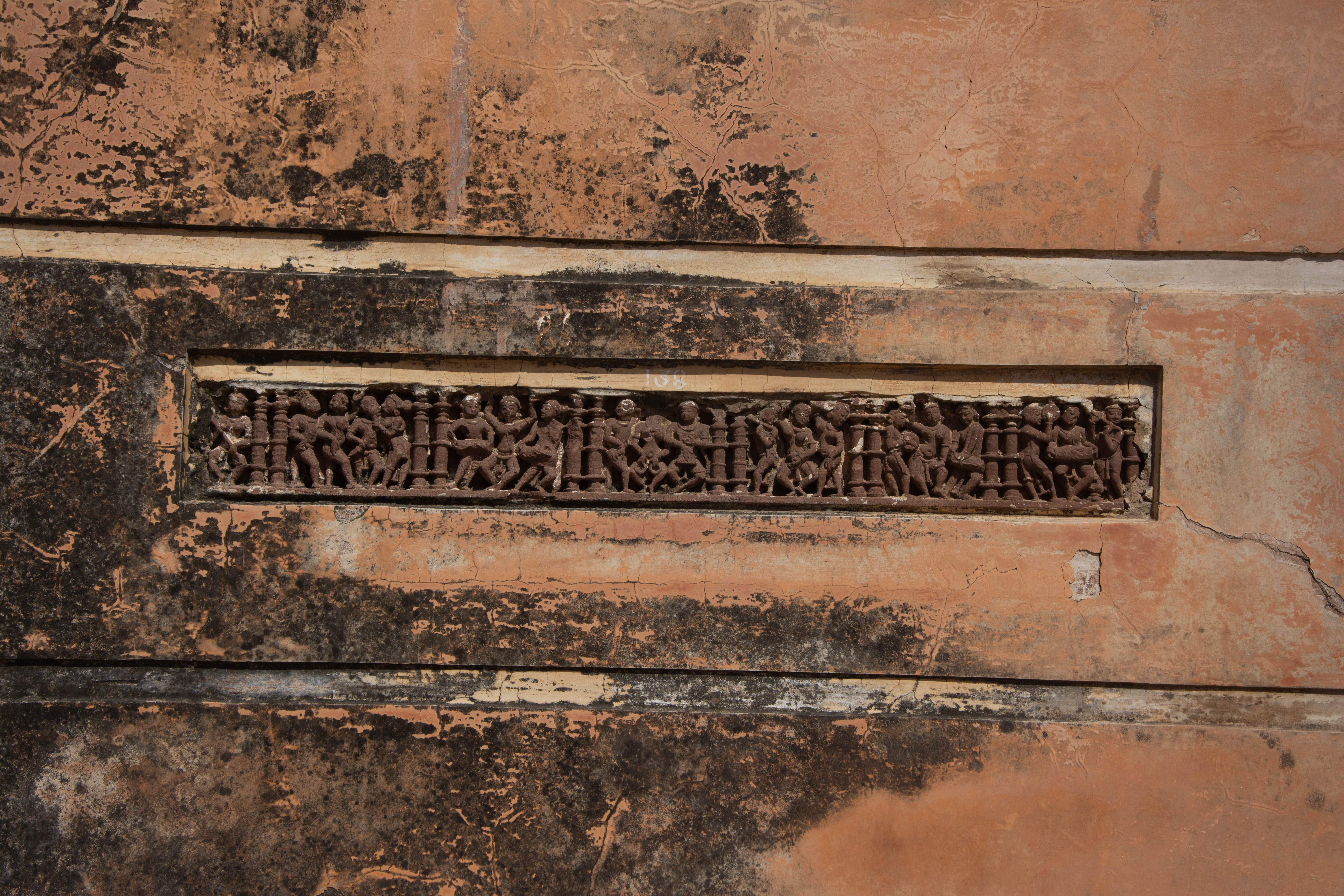 The Shiva Temple of the 18th century CE features a red sandstone panel with various segments separated by pillarlets, each containing various musicians and dancers.