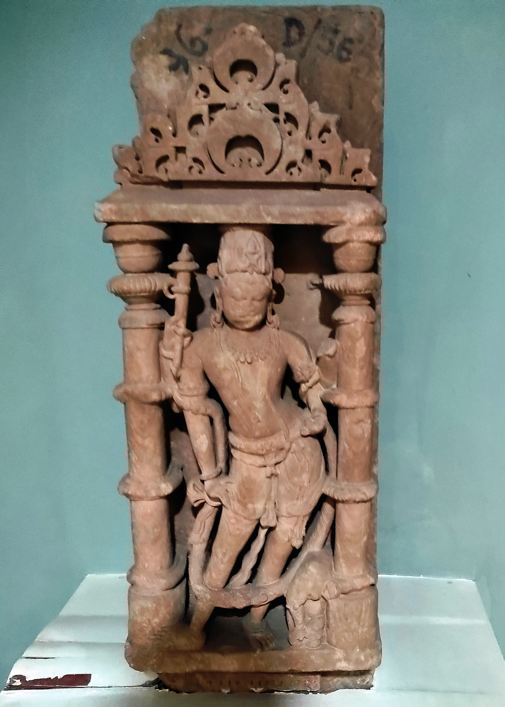 A four-armed Indra placed inside a devakostha-niche, easily identifiable by his vahana, an elephant. The Government Museum in Sikar now houses the loose architectural fragment from Harsha Hill. Despite the broken nature of the two hands on the left side, the upper right hand clasps an ankush, while the lower hand rests gracefully on his right leg.