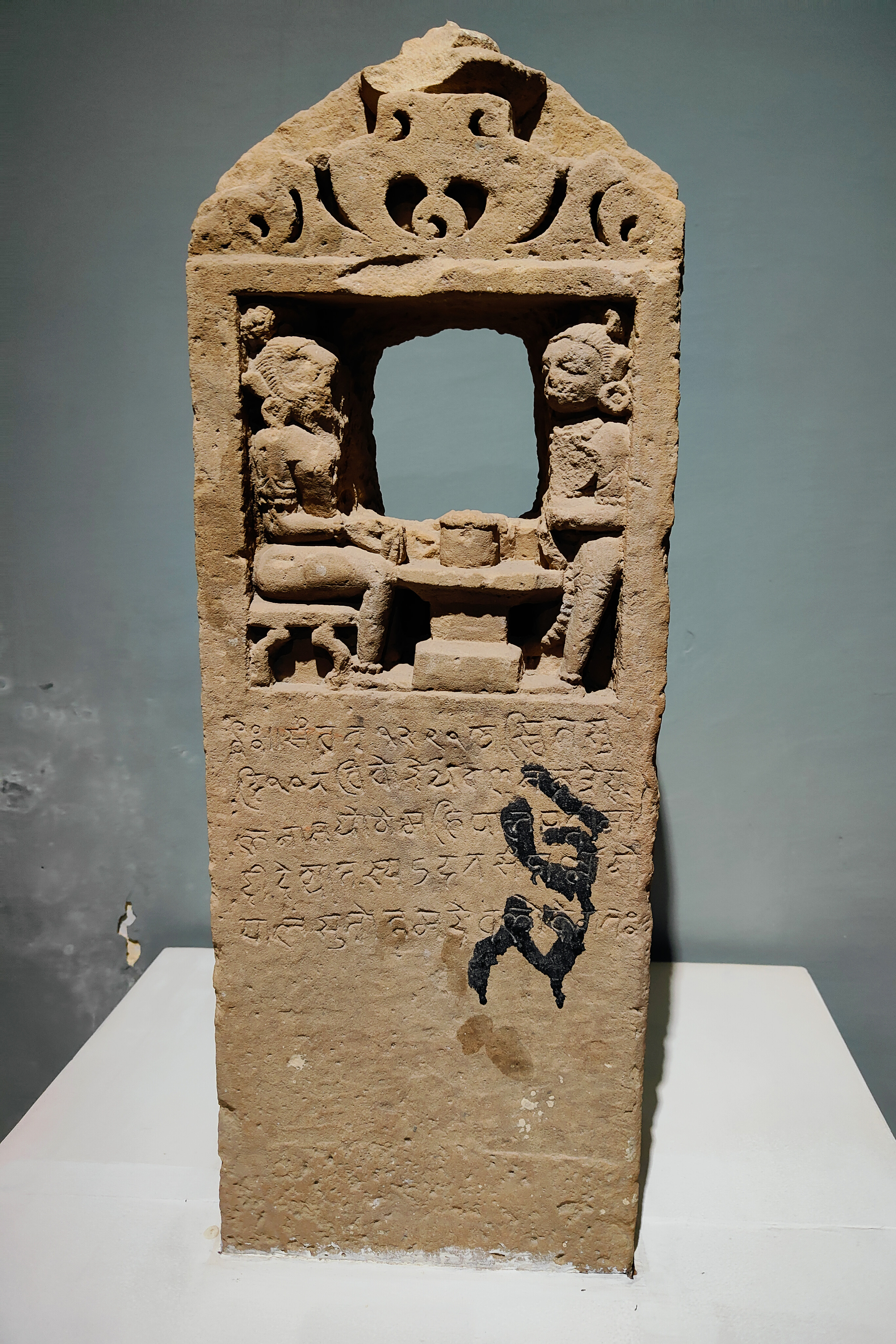 The memorial stone in the Government Museum Sikar bears an unpublished epigraph recording the death of an individual named Mahipal. The panel's top features a niche that depicts a Shaiva ascetic on one side of a shivalinga and a devotee, possibly Mahipal, on the other.