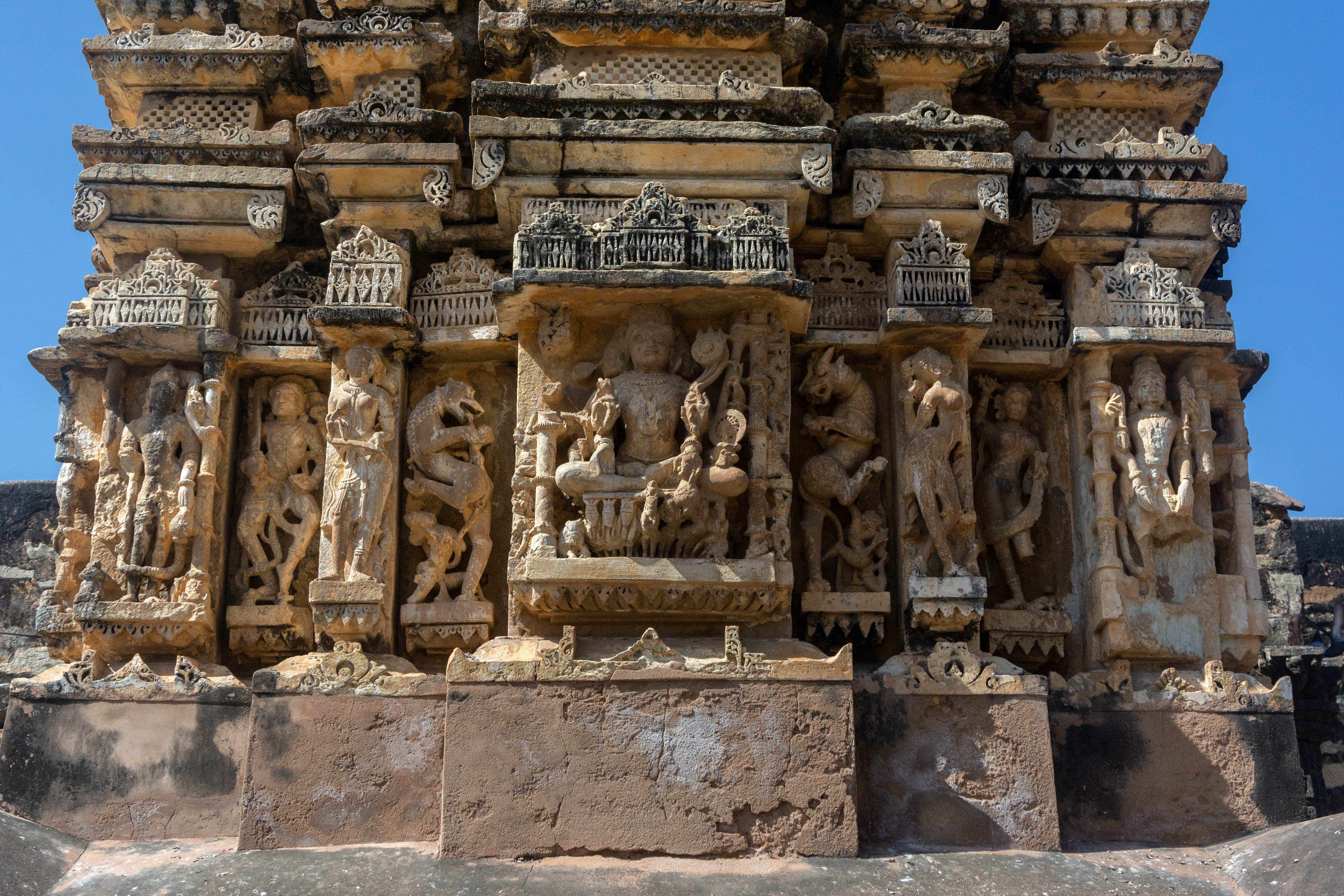 Image 3: This is the east-facing elevation of the central shrine in the Neelkanth Mahadev Temple. The Harihararka (or Hariharapitamaharka), a unique composite image on the exterior wall facing east, incorporates Shiva, Vishnu, Surya, and plausibly Brahma into a single sculpture. Sitting on a chariot of seven horses, the three-faced figure embodies the attributes of all its representative deities.