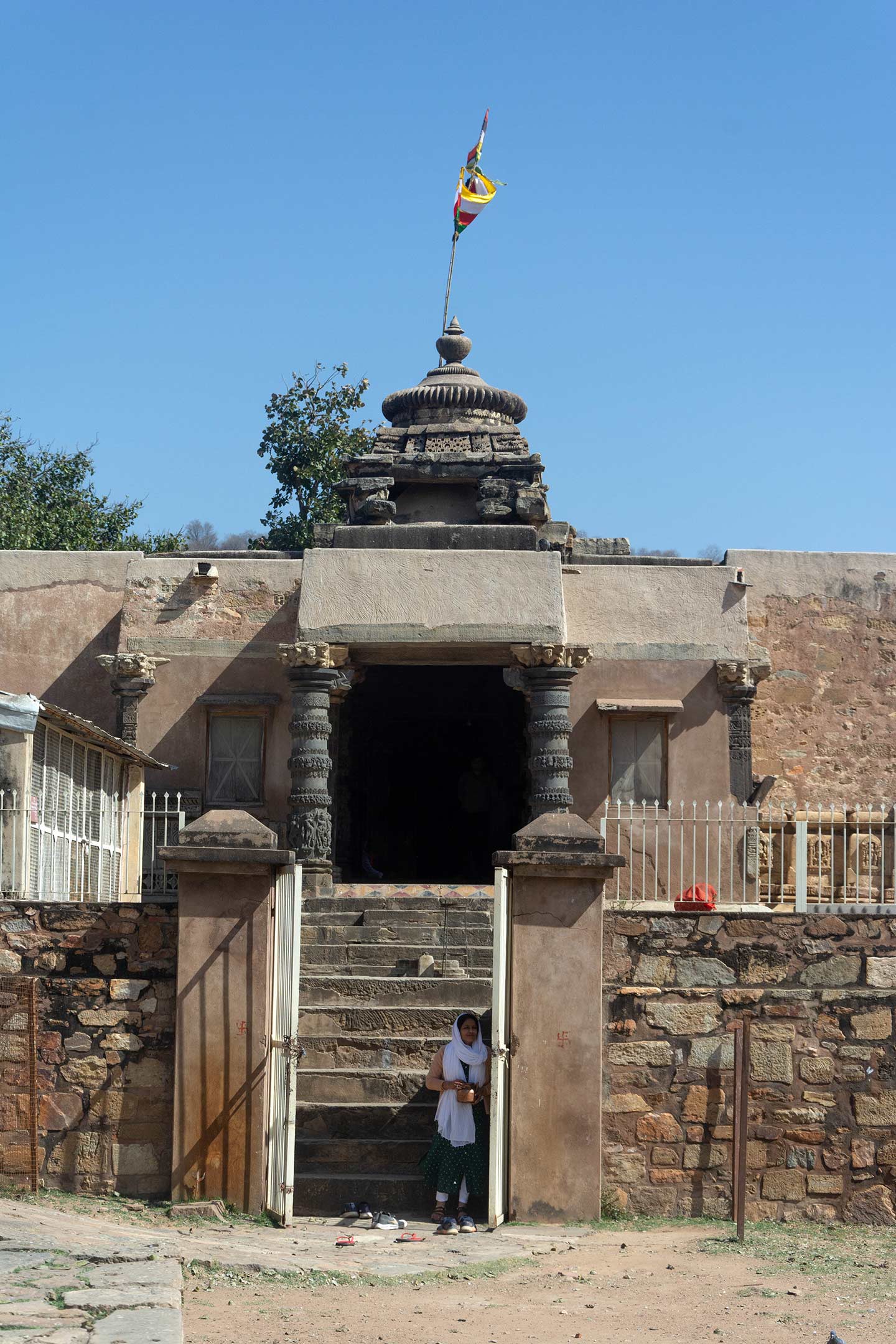 The picture shows the west-facing entrance of the Neelkanth Mahadev Temple. The temple stands on a plinth. It is accessed through a gate built into a later-added boundary wall.