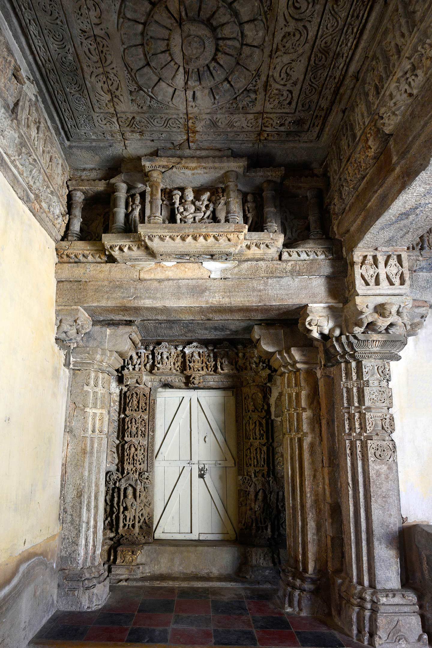 This is a view of the entrance to the southern shrine, which is one of the three shrines in the Neelkanth Mahadev Temple. An ornate dvarashakha (door jambs) adorns the entrance. The passage's ceiling, which connects to the shrine, is a flat ceiling with a lotus medallion. It depicts Shiva and Parvati on the latatabimba (lintel) of the dvarashakaha. The pilasters at the entrance of the passage to the shrine are relatively simple, compared to the central pillars of the mandapa (pillared hall).