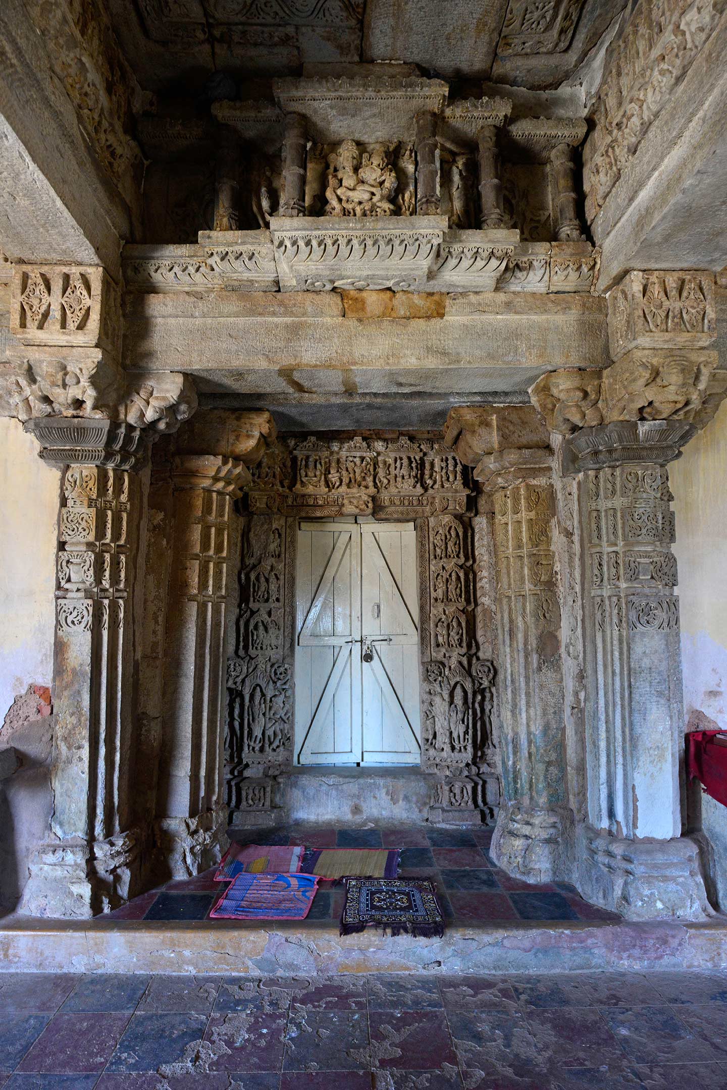 This is a view of the entrance to the northern shrine in the Neelkanth Mahadev Temple. Both the north and south shrines have identical dvarashakhas (door jambs), except for the deity couple above the lintel beam supported on the shrine's pillars. The shrine depicts Vishnu Lakshmi seated on Garuda. Deep niches, similar to those on the exterior walls of temples, adorn the lintel containing the Vishnu Lakshmi sculpture.