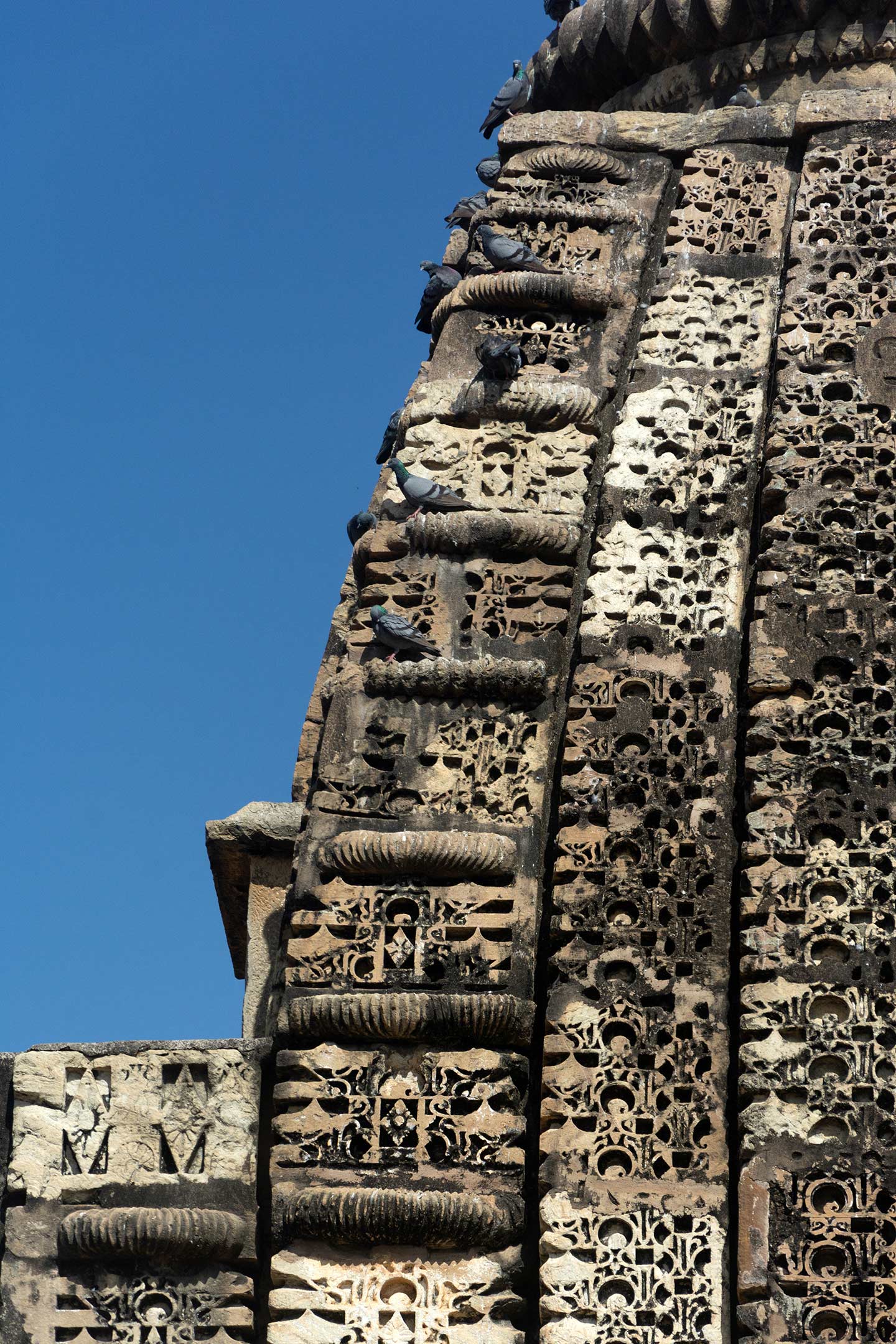 Seen here are the details of the Latina nagara (mono-spired) shikhara (superstructure) of the central shrine in the Neelkanth Mahadev Temple. The structure consists of five vertical projections. The central band, or madhyalata, is flanked by pratilatas. These three bands are made up of a mesh of gavaksha (dormer window) motifs. The corner bands of the shikhara feature aedicules known as bhumikhandas, which again feature gavaksha designs on their surfaces. Flat ribbed discs separate these aedicules, which diminish in size. This shikhara suggests that the Latina nagara shikharas at the temple's other two shrines must have been similar.