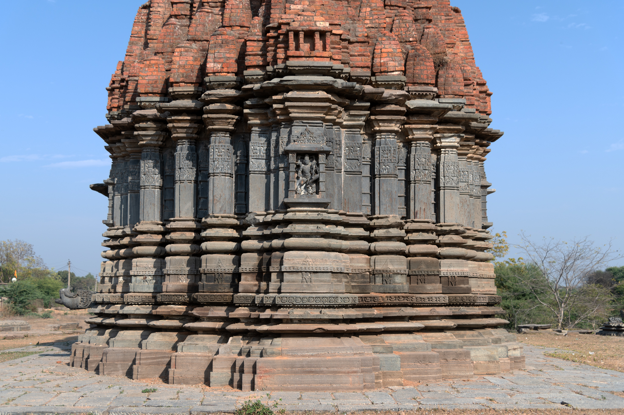 This is the west-facing elevation of the main Mandaleshwar Mahadev Temple. The temple's mulaprasada (main shrine) is saptaratha (consisting of seven projections). The intermediate and corner projections of the temple are slender and narrow, devoid of any sculptures. Only the central projection has a sculpture in a niche.