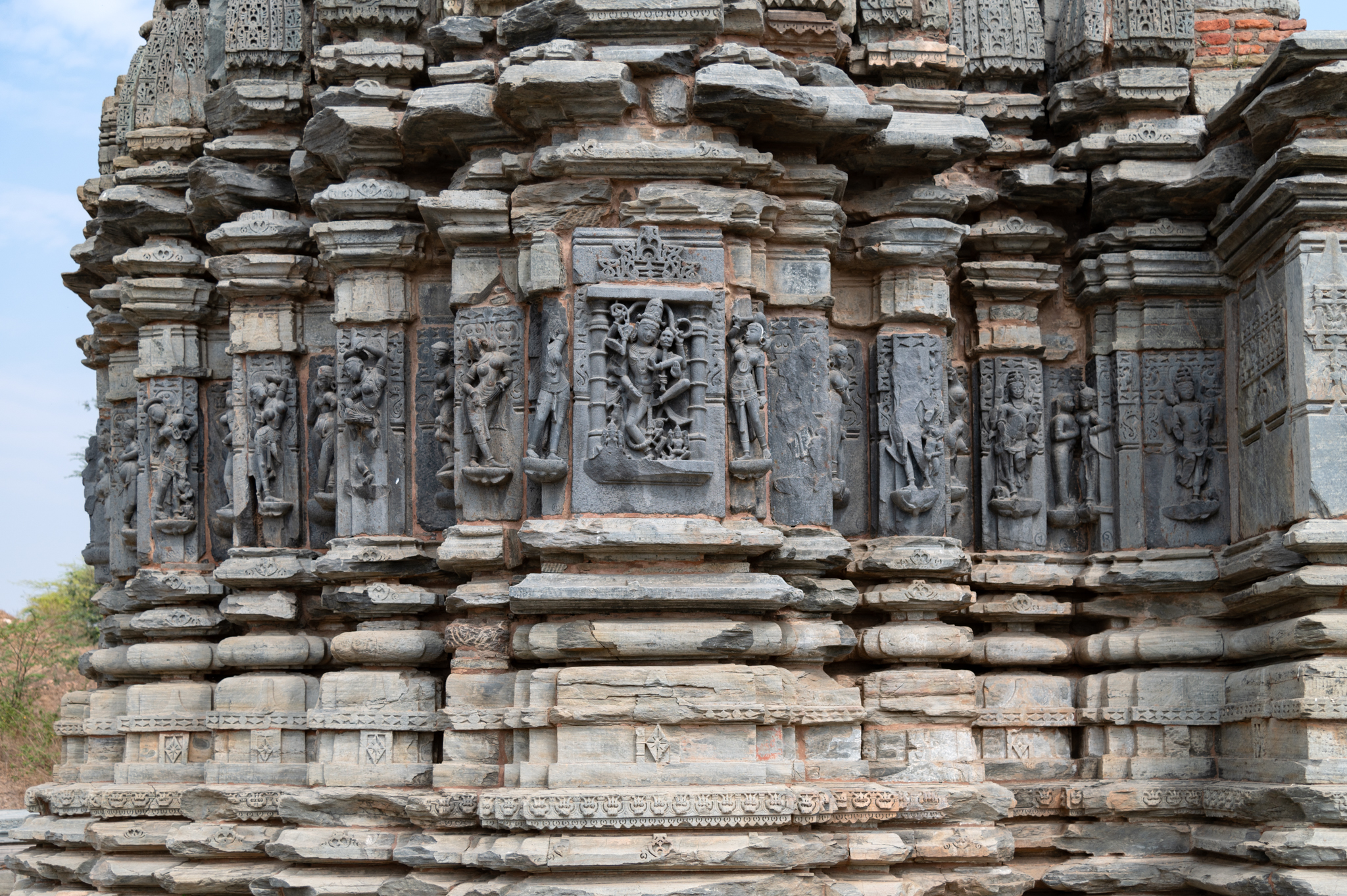 The temple's vedibandha (basal mouldings) include graaspatti (band of kirtimukhas or face of glory), kumbha (pot) with a diamond motif, kalasha (a pitcher), and kapotali (cyma recta). Images of gods, goddesses, apsaras (celestial damsels), and ascetics adorn the entirety of the wall projections, built in schist stone. These consist of the Shaiva images—Natesha, Andhakasura, and Chamunda—inside the principal niches and dikpalas, i.e., the cardinal deities—Indra, Agni, Nritti, Vayu, Kubera, and Isana. The wall design scheme with deities on the bhadra (central projections), dikpalas on the karna (corner projections), and salilantaras with apsaras is a common pattern in the regional temples.