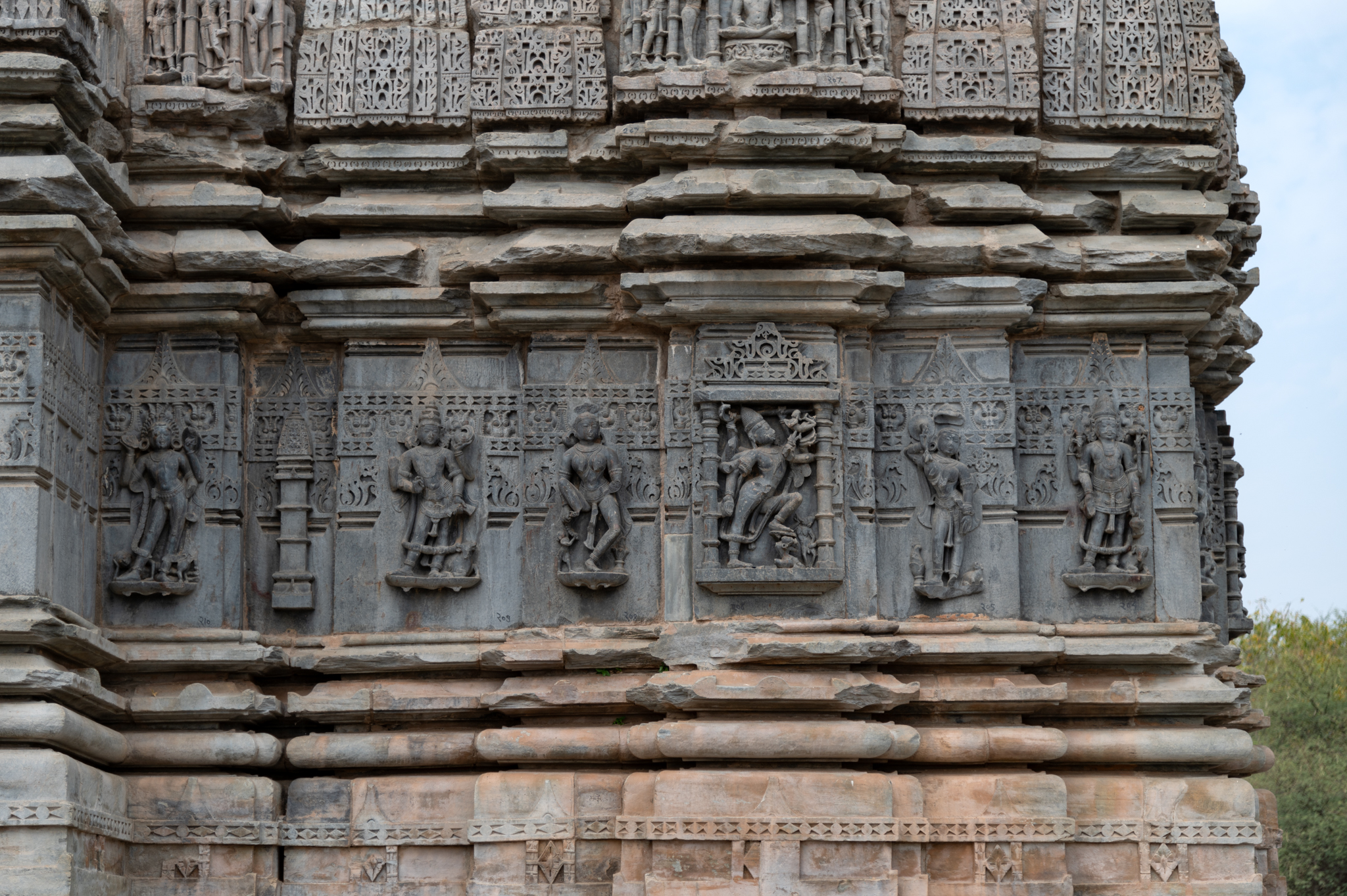 This is the south-facing exterior wall of the Shiva Temple. Sculptures adorn all the wall projections. The bhadra (central projection) has a sculpture of Tripurantaka Shiva, the intermediate projections have surasundaris (celestial damsels), and the corner projections have dikpalas (deities for cardinal directions). The jangha (wall) portion of the temple is made of a different stone than the rest of the temple. Except for one recess between the wall of the shrine and the mandapa (pillared hall), recesses separate the projections from each other.