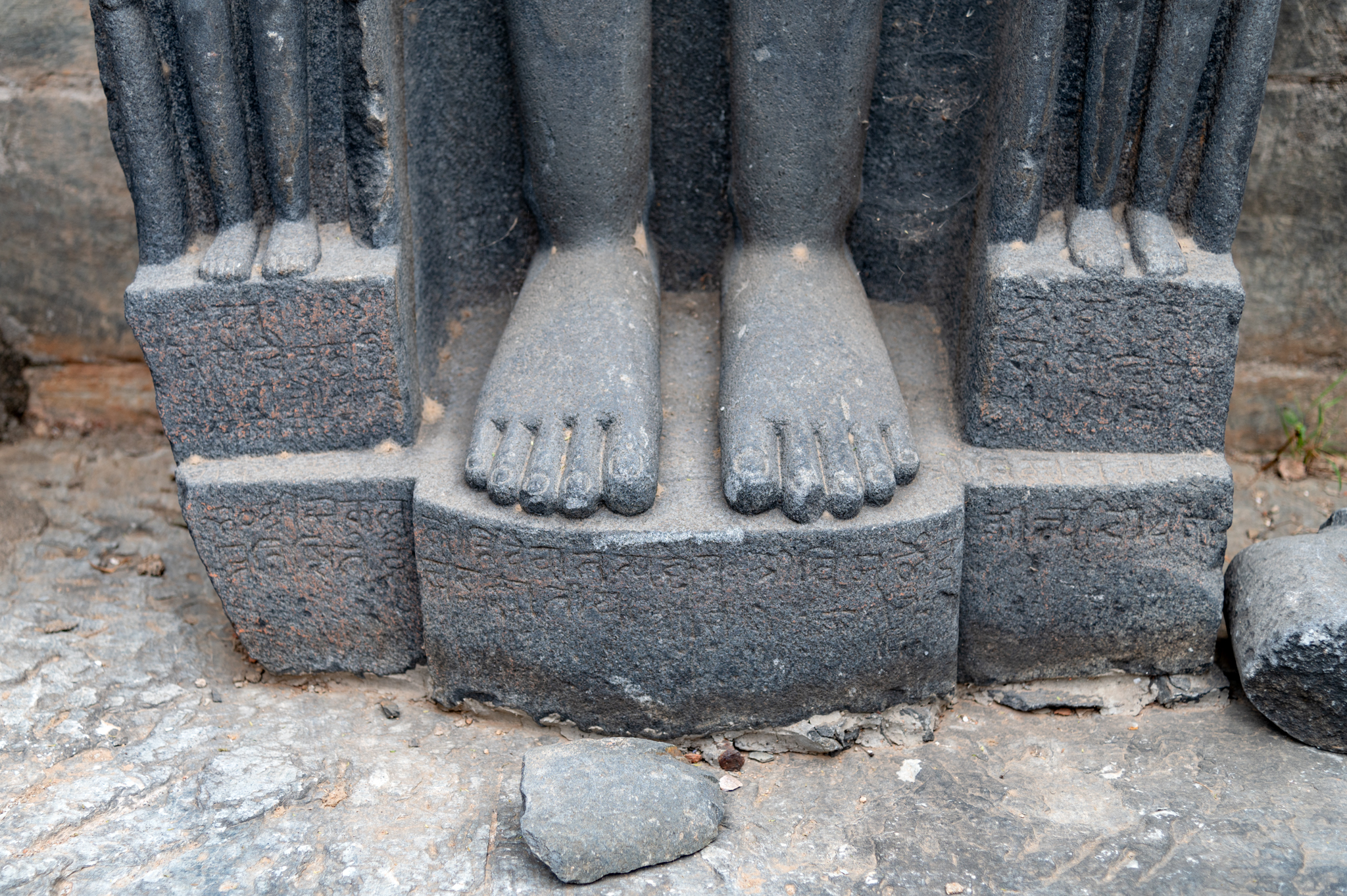 This is a colossal sculpture of a Jain Tirthankara standing in kayotsarga (dismissing the body) posture, found in the ruined shrine. 16th-century inscriptions adorn the pedestal of the Jina Tirthankara sculpture, located in the ruined shrines to the west of the main Jain Temple. A cursory glance at the orthography and script of the inscriptions indicates that they belong to the 16th century, probably recording the sculpture's consecration. To the west of the central temple, the pedestal divides the inscription into four parts. The inscriptions at the base of the free-standing statues date from the 16th century CE. Black stone, primarily granite, forms the sculpture's carving.