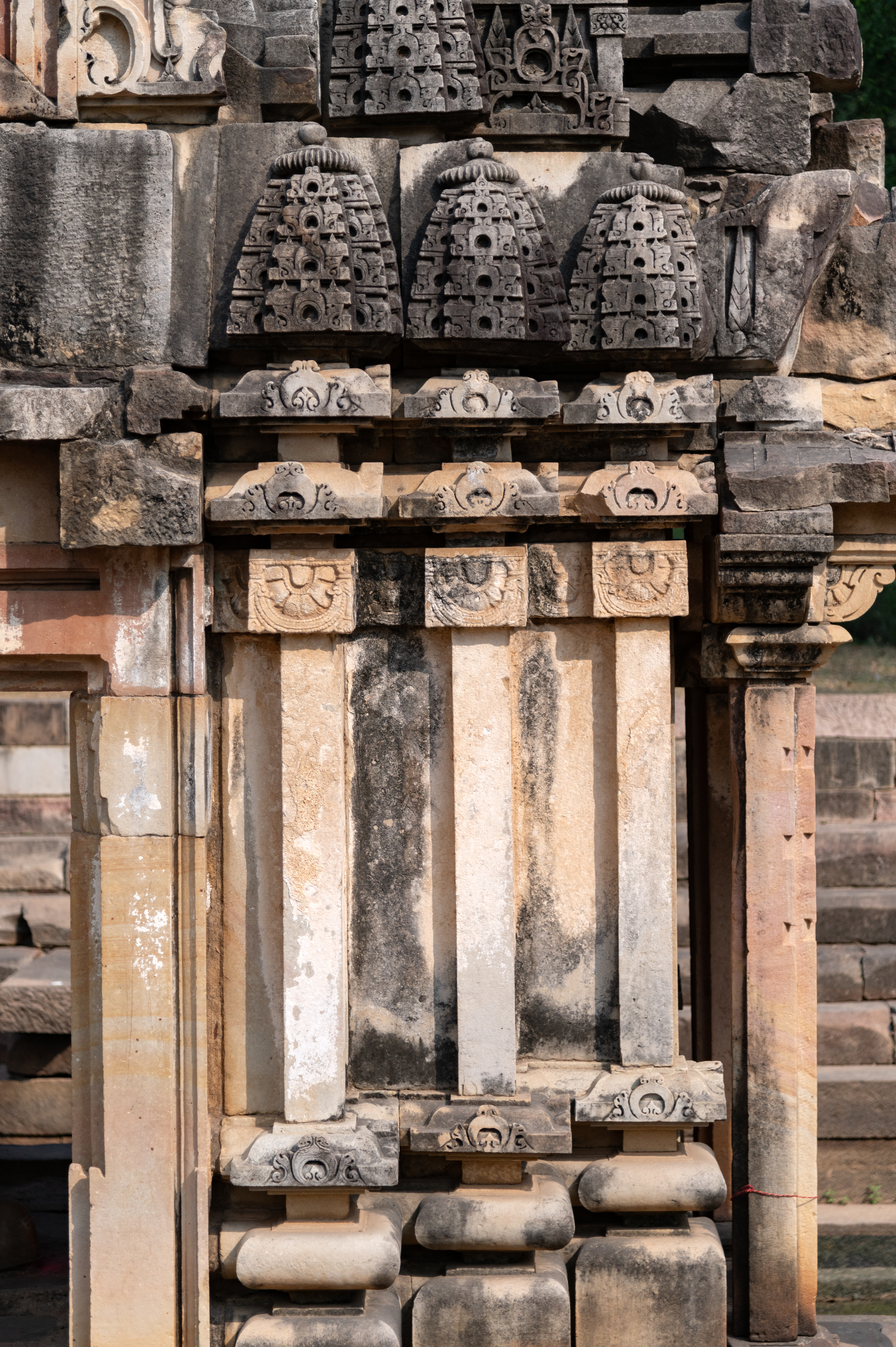 The jangha (wall) of the Shiva Temple (Temple 3) features plain pilasters projecting out of the surface, while the top portion is adorned with an ardhapadma (half-lotus motif) enclosed by a garland loop. Above the jangha, a varandika (moulded parapet) is placed, which features the antarapatta (recesses between mouldings) between two kapotapalikas (cyma recta moulding). Above the varandikas, miniature shikharas (spires) are placed which creates the anekandaka shikhara (multispired superstructure).