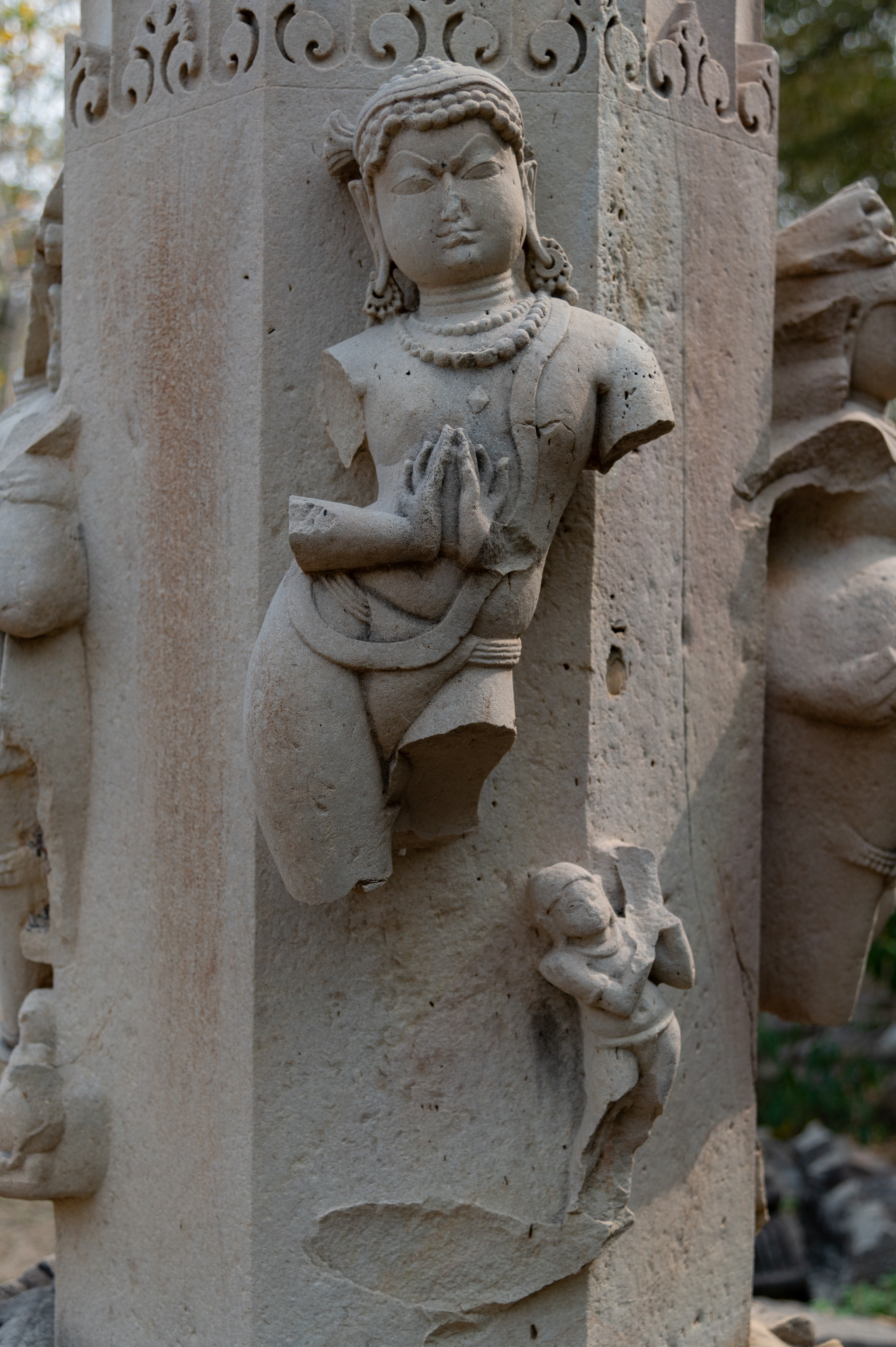 The male figure on the other pillar of the torana (ornamental gateway) is depicted in the same posture with folded hands. He is also adorned with heavy jewellery and bears the distinctive mark of Jaina deities on his chest. He is accompanied by an attendant.