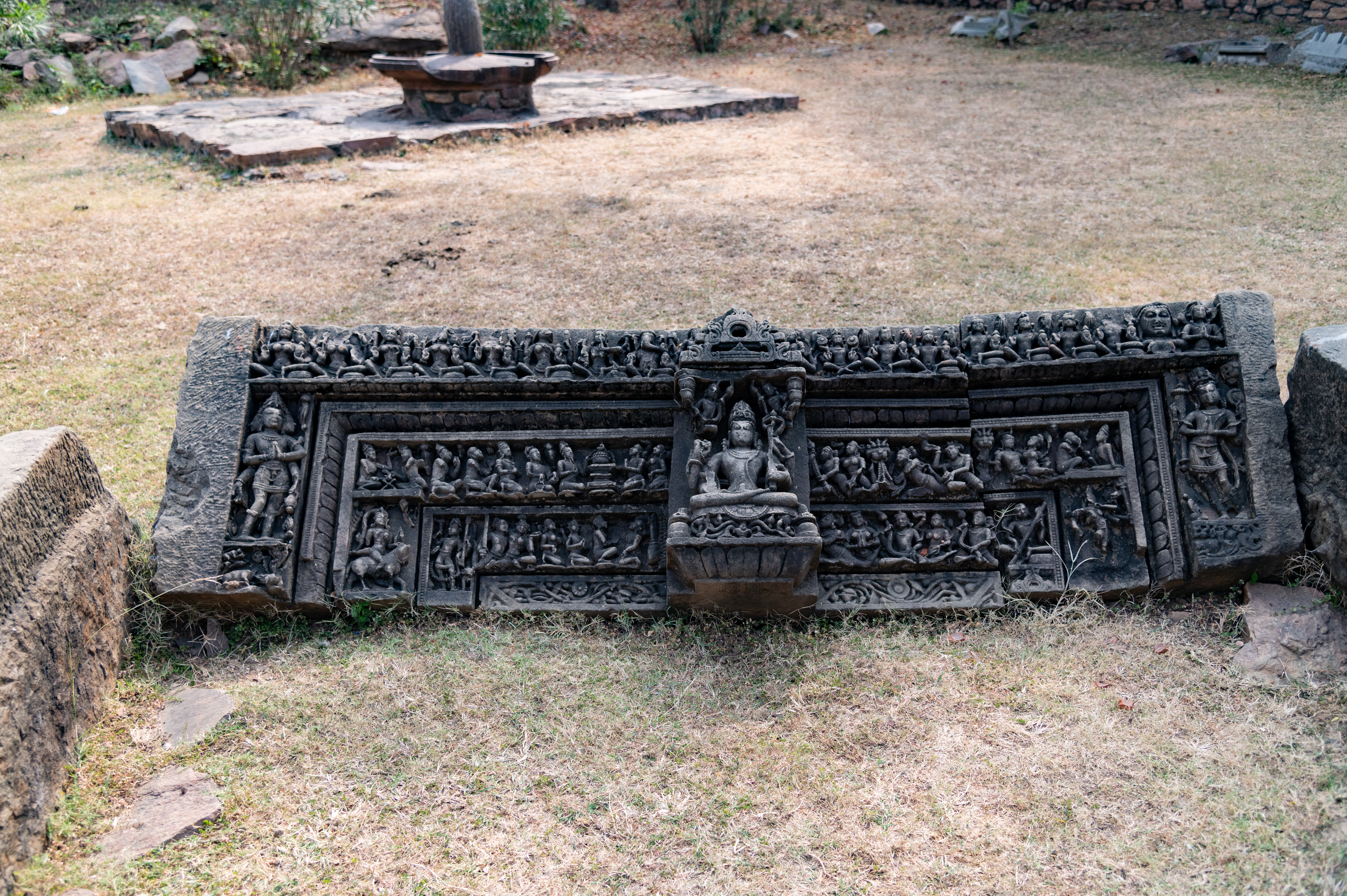 The lintel of the doorframe depicts a seated, four-armed Shiva at the centre. On the proper right of the torana (ornamental gateway), a three-faced Brahma is shown standing, folding hands in veneration. On the other side, Vishnu is shown standing, holding a gaya (mace) and a chakra (discus) in his upper hands, while his front arms are joined in anjali hasta, in veneration to Shiva. Between these three divine figures, four horizontal bands are carved depicting gandharvas (celestial musicians), devotees, and ascetics worshipping the linga. At the topmost band, on the proper right side, matrikas (mother goddesses) are depicted along with Ganesha, while on the proper left side, navagrahas (nine planets) are represented.