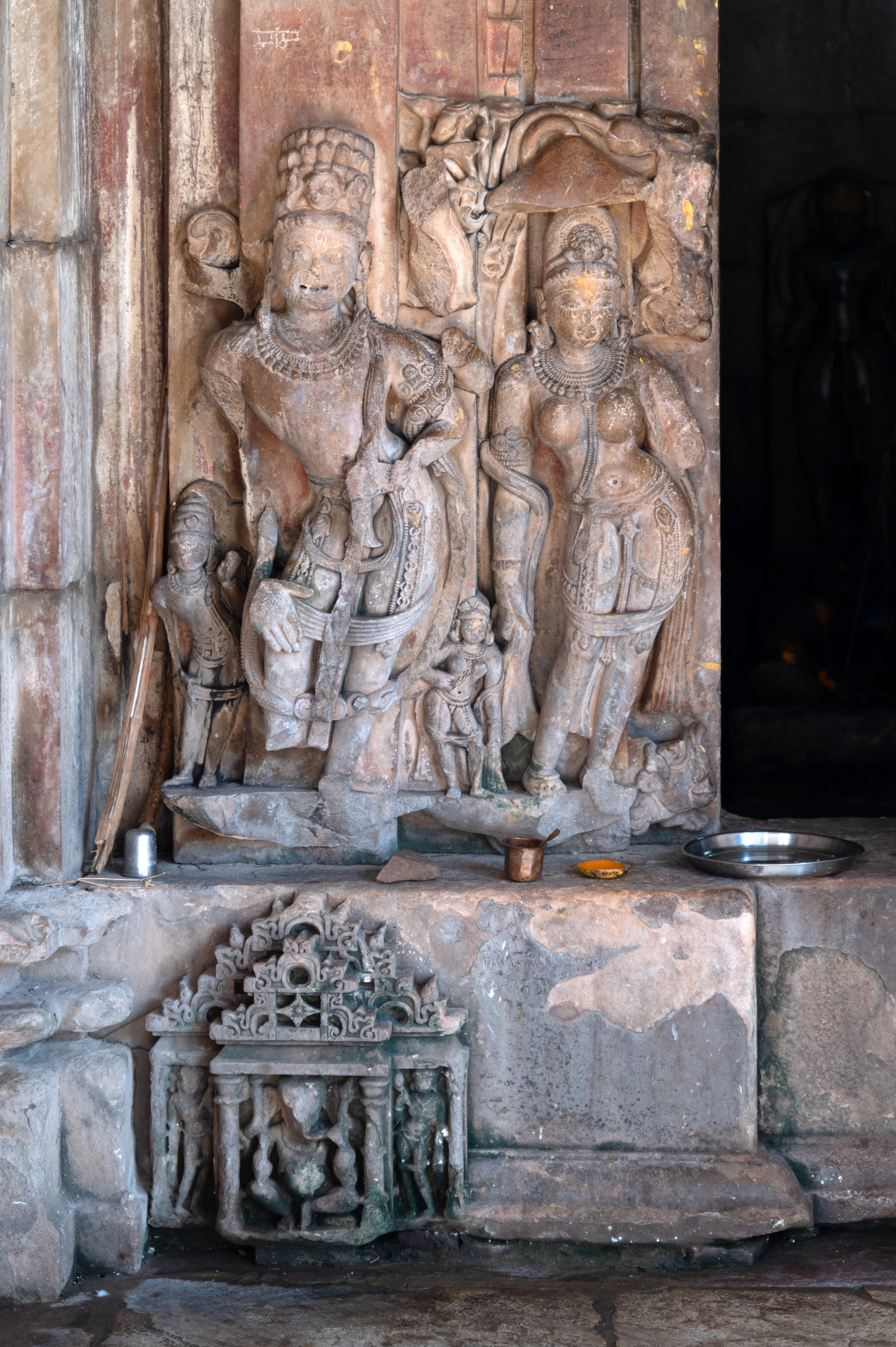 The bottom of the garbhagriha (sanctum sanctorum) door frame is decorated with the figures of the river goddesses and dvarapalas (door guardians). On the proper right side of the doorframe, the river Goddess Ganga is represented. The Goddess is shown standing on a pedestal with her vahana (mount), a makara (crocodile), depicted behind the pedestal. She is heavily bejewelled and has a canopy of inverted flowers. Next to her stands a four-armed dvarapala, with all arms broken. He has a beard, and his jatas (matted hair) are neatly arranged in layers, and his two attendants are depicted alongside him. At the bottom, a niche is carved, which is installed with the figure of Ganesha.