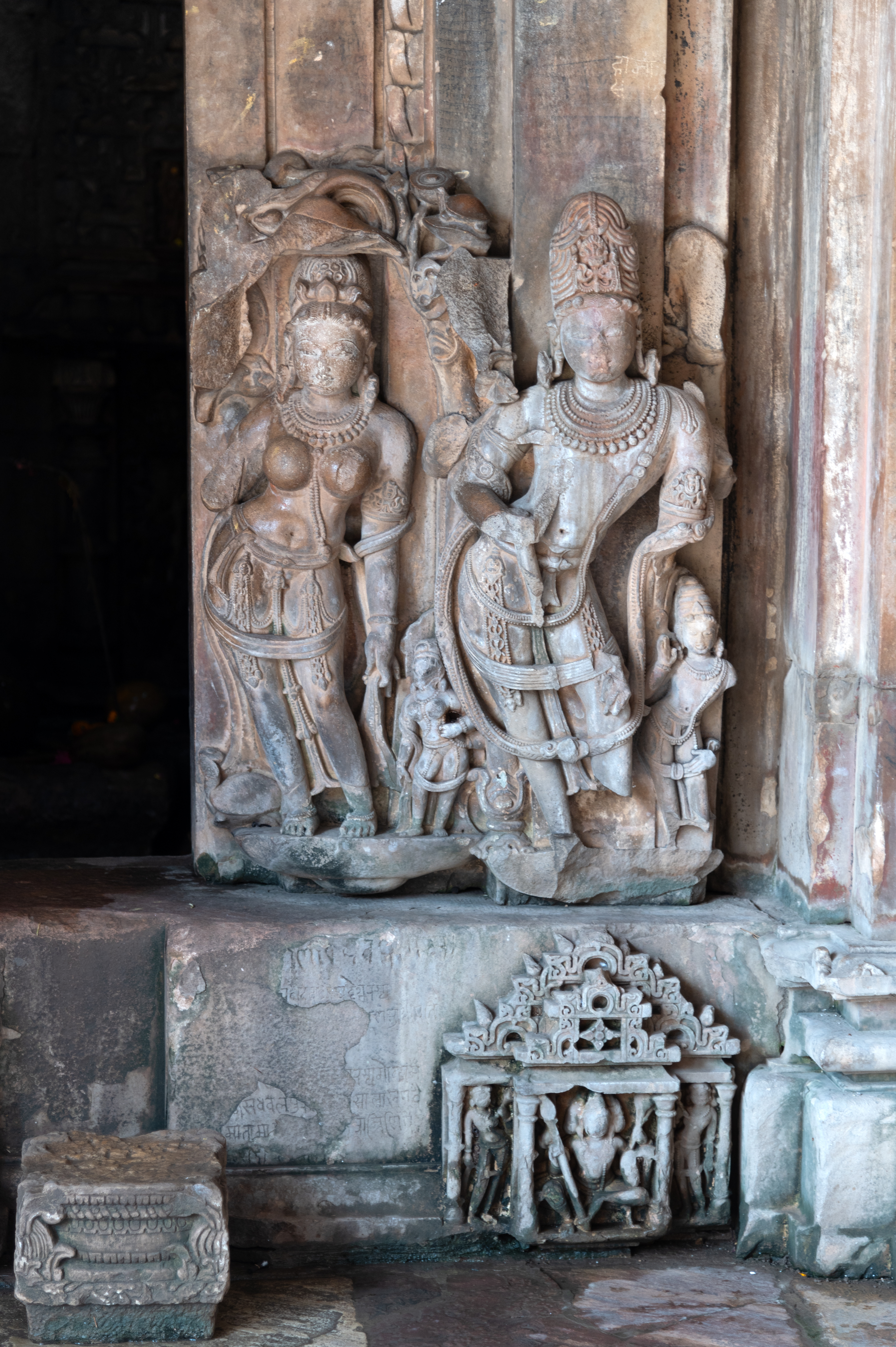 On the proper left side of the doorframe, the river Goddess Yamuna is depicted standing on a pedestal, with her vahana (mount), a kachhapa (tortoise), shown on the same pedestal. Next to her, a Shaiva dvarapala (door guardian) is depicted with his two attendants, one male and one female. Beneath this, a niche is carved, featuring a figure of Kartikeya with three heads, holding his weapon, the spear, in front.