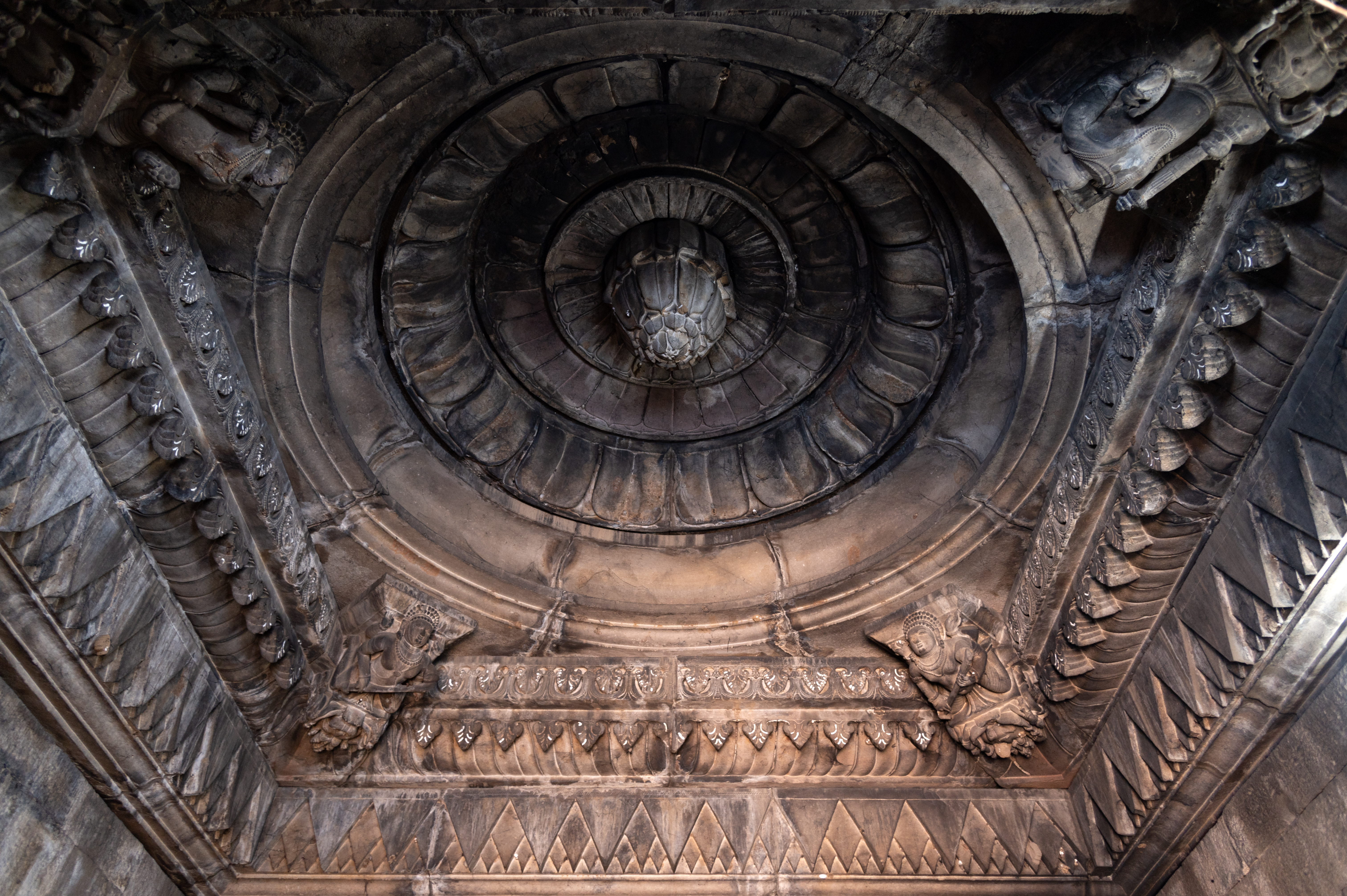 The garbhagriha (sanctum sanctorum) is comparatively plain and simple, except for the ceiling, which has a square shape with four-armed bharavahakas (weight bearers) positioned at each corner. Their upper arms are raised upward to support the roof, while their lower arms carry weapons and an attribute. The square shape of the ceiling transitions into a circle, resembling a full-blown lotus, with a lotus bud hanging from the centre.