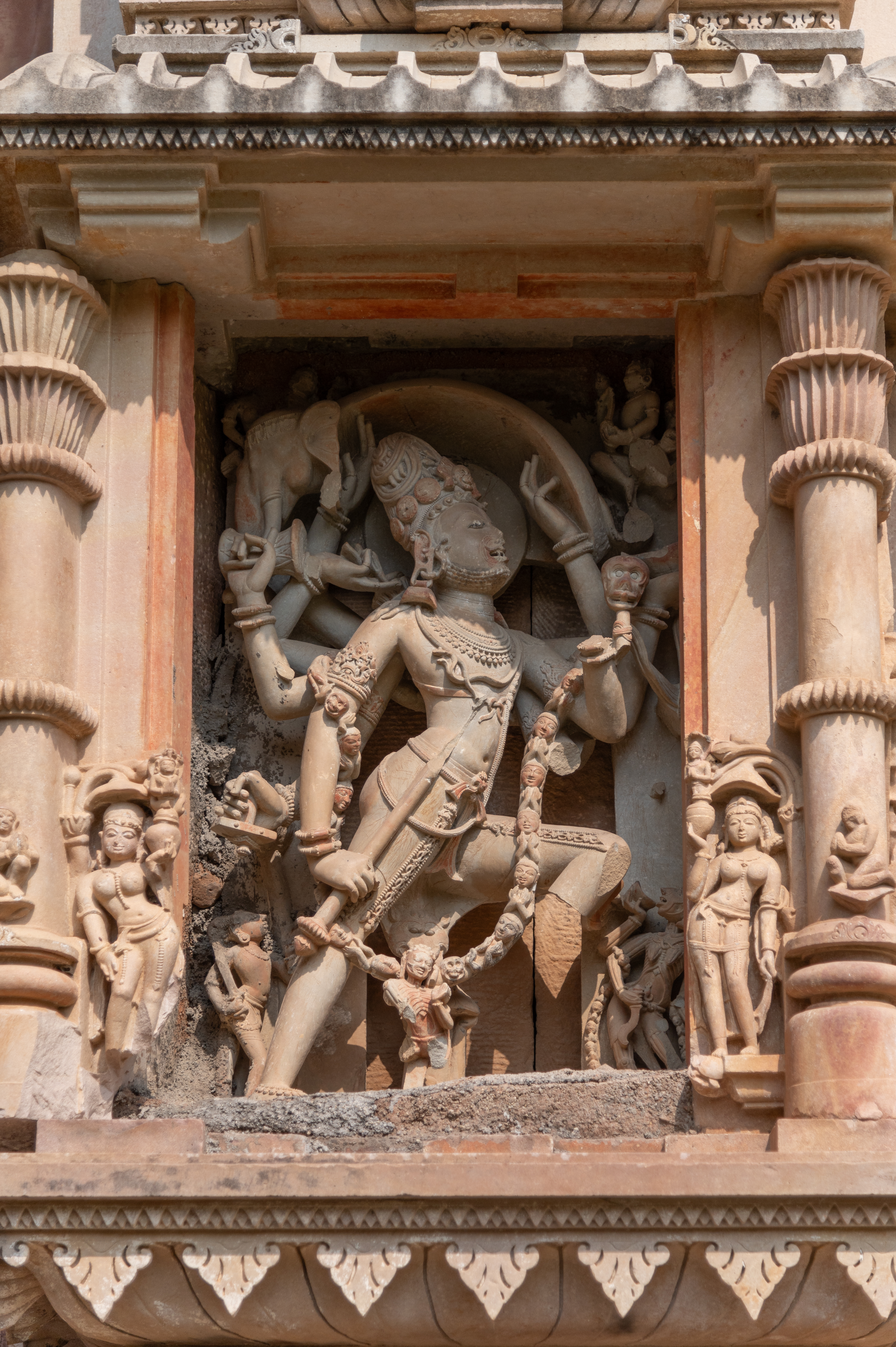 One of the most beautiful and eye-catching sculptures of this temple is situated on the southern wall of the garbhagriha (sanctum sanctorum) in the bhadra (central offset). It depicts Shiva in the form of Andhakasurvadha, holding various attributes in his multiple arms. He is carrying a broken weapon, which could be a trishula (trident), and is depicted holding the head and skin of a gajasura (a demon in disguise of an elephant). There are three small figures at the bottom of the panel, out of which one is Chamunda, on his left, shown drinking from the bowl.