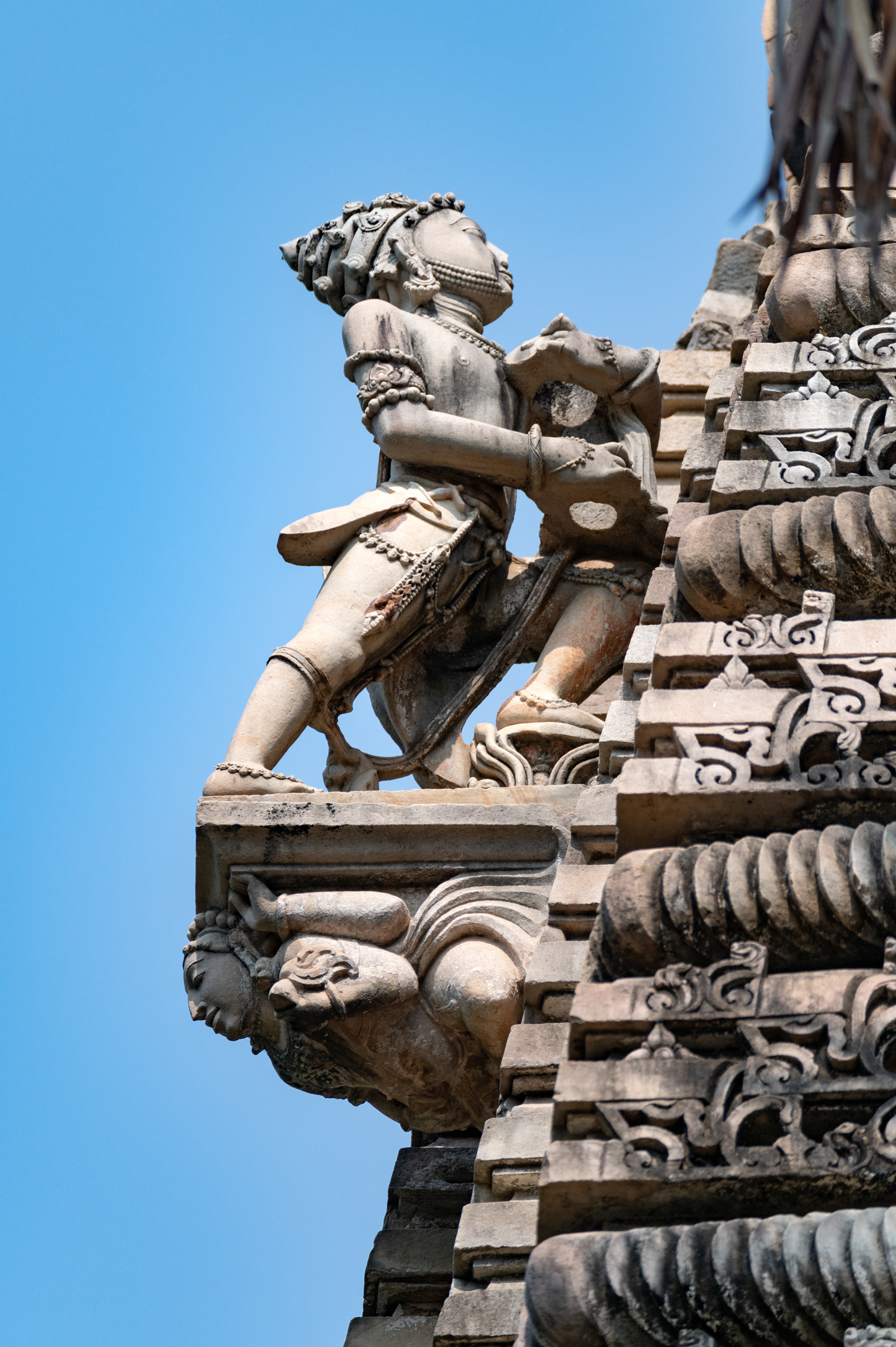 One of the most interesting sculptures is of a dhvaja vahaka (flag bearer), placed at the shikhara (superstructure) of the garbhagriha (sanctum sanctorum). The bearded male figure is shown standing, facing the shikhara, with one leg placed on the floor and the other placed on a lotus pedestal. He is wearing a crown and is heavily adorned with jewels. He is carrying a sword, which can be seen hanging from his waist. His hands are shown one above the other, holding a hollow circular disk, which must have been used to hold the dhvaja (flag) of the temple.