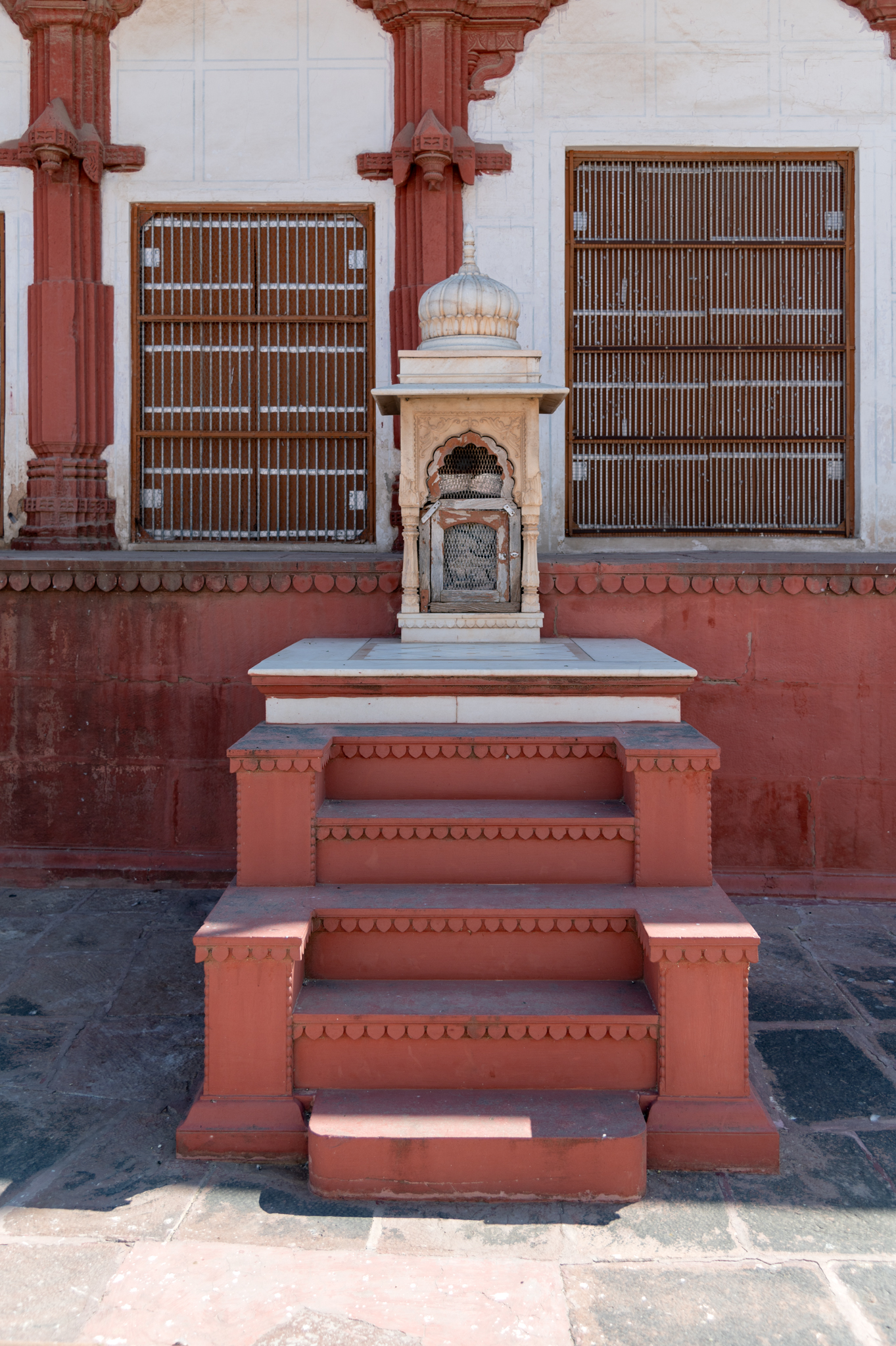 A closer view of the small chhatri, which is attached to the plinth of the temple. This chhatri is probably a memorial which was built here at a later date. It is made of marble stone, and the steps connected to its pedestal are painted in the same manner as the main temple plinth.