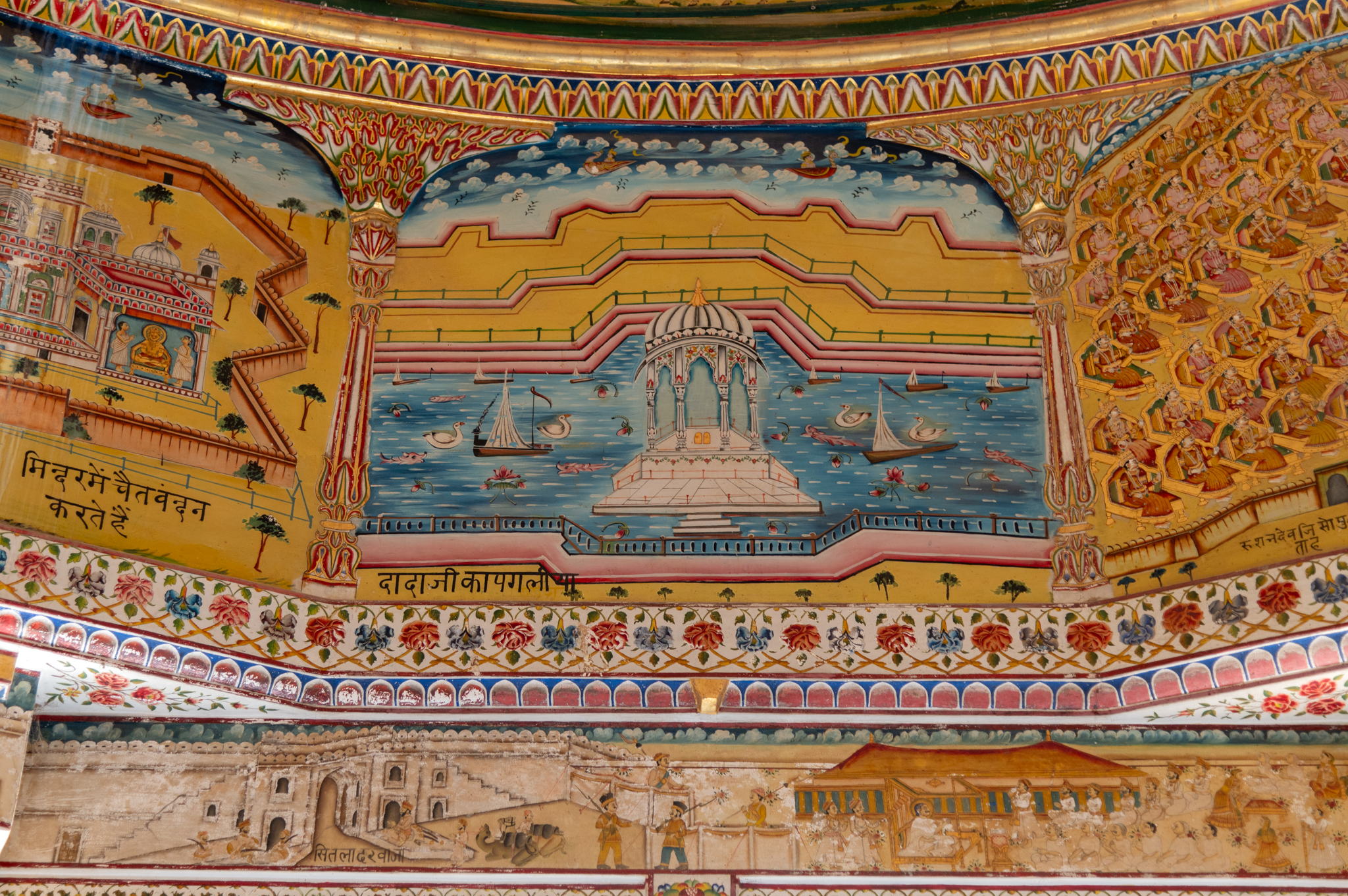 The painting of ‘Dadaji ka pagaliya’ depicts a semi-upon chhatri, which is usually built as a memorial of the deceased. It is painted on the ceiling of the mandapa (pillared hall) of the Bhandasar Temple. There is a chhatri (memorial) painted in white, likely to resemble the marble construction. A water body surrounds it. On the open pedestal of the chhatri, there are two footprints. Dadaji in this painting could be a reference to one of the four Dada Gurus of the Jain tradition, namely, Jinadatta Suri (1075-1154 CE), Jinachandra Suri Manidhari (1140-1166 CE), Jinakushala Suri (1280-1332 CE) and Jinachandra Suri II (1541-1613 CE). Their memorials are often found next to Jain temples.