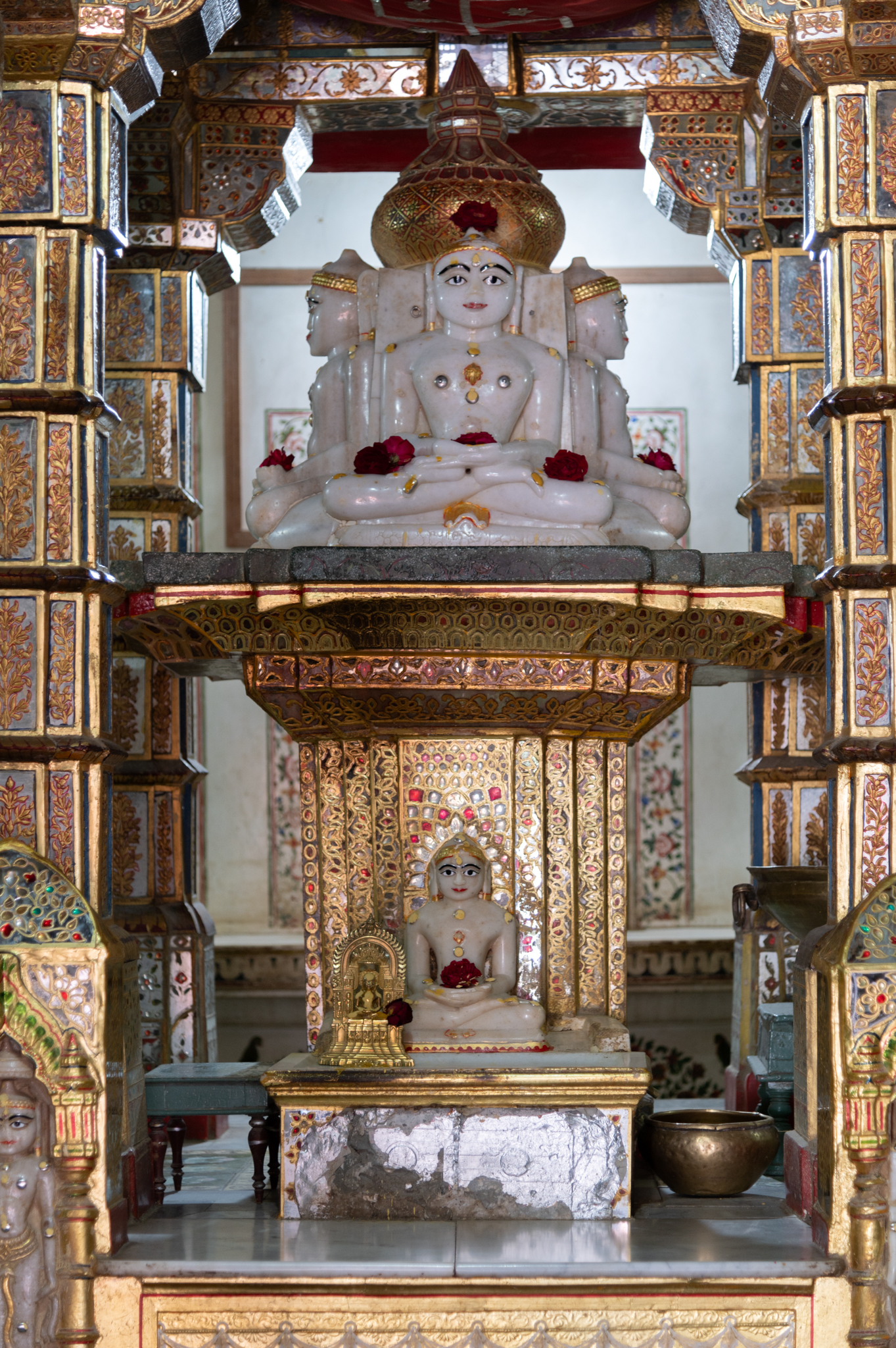 The enshrined image of Sumatinath, the fifth Jain Tirthankara. The sarvatobhadra (open from all four cardinal sides) sculpture of Sumatinath is placed on a high pedestal. The sculpture sits on a low platform having a motif of a Krauncha (bird), which is lanchan (emblem) of the Tirthankara carved at the centre. The pedestal of the sculpture is adorned with gold embossing meenakari (enamel) artwork. On the front side of this pedestal is another sculpture, probably of another Tirthankara. The enshrined object is under a canopy supported by four pillars. All the sculptures are made of marble with ornamentation in red and gold colour. There are also some small portable sculptures of Tirthankara in the garbhagriha, probably donated as votive images.