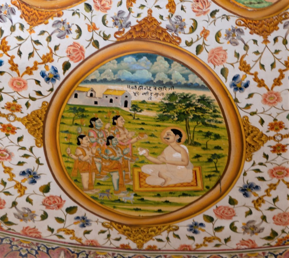 The tenth oval painting (in clockwise order) in the lower/outer circle in the ceiling of the mandapa (pillared hall) is an episode from the life of Jinadatta Suri. It is said that he subdued the bavan (fifty-two) Bhairava pirs (spiritual guides), who eventually became his servants. Jinadatta Suri is shown sitting in a van (forested area), and the four pirs representing the fifty-two Bhairava pirs are dressed like Hindu deities. As suggested by Lawrence Babb, this is indicative of the tussle between two religious factions, the Jains and the Shaivas. The inscription reads, ‘Shri Jinadatta Suri Ji 52 bir bulaye.’