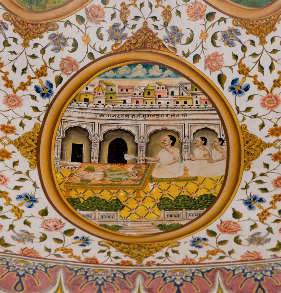 The story in the sixteenth oval painting (in clockwise order) in the lower/outer circle in the ceiling of the mandapa (pillared hall) revolves around Jinadatta Suri, probably depicting how he saved a drowning ship. The acharya (those who impart knowledge) is sitting on the banks of the water body, accompanied by three disciples. The ship in the water has an elephant head, and a person in Rajasthani attire is seated on the ship. The water contains aquatic flora and fauna, such as fish and lotus flowers. The inscription reads, ‘Shri Jinadatta Suri ji ne nevai dari.’ The most interesting aspect of this painting is the name of the artist, M. Altaf, inscribed at the bottom of the oval border of the painting.