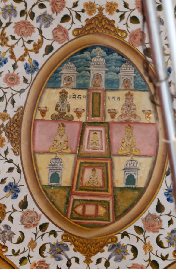 The painting in the inner/upper circle in the ceiling of the mandapa (pillared hall) has Mount Meru, the sacred mountain, depicted in the cosmic universe. There are five stages, from bottom to top, that symbolizes the centre of the world, which is surrounded by Jambudvipa, the earthly world. After every Tirthankara is born, he meets with god by ascending all these stages. Mount Meru painting illustrated the journey of the Tirthankara; hence, the centre of every stage has a Tirthankara sitting in a padmasana (lotus pedestal) pose. The inscription reads, ‘Meru Parbat.’