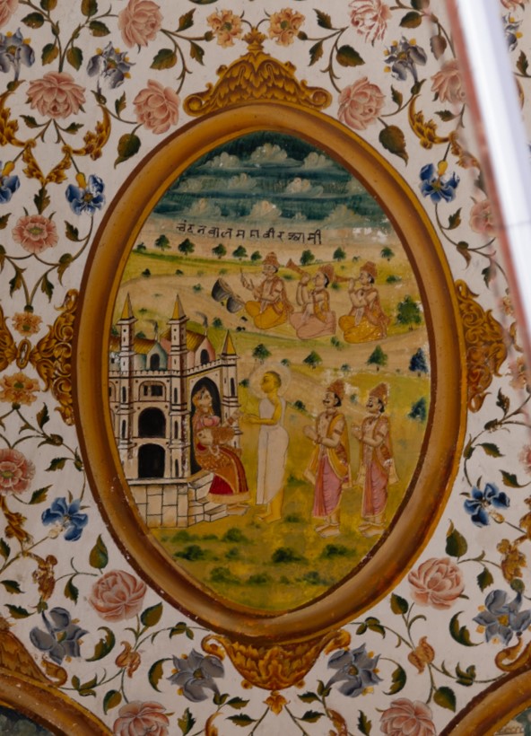 The story of the painting in the inner/upper circle in the ceiling of the mandapa (pillared hall) revolves around Mahavir Swami's stringent fasting conditions, which required specific circumstances for accepting food. Chandanbala, formerly known as Princess Vasumati, fulfilled these conditions despite enduring hardships as a slave after being separated from her royal family. The haveli (mansion), in which the princess is depicted sitting, reflects significant European architectural influence. Mistreated by a merchant’s wife, Chandanbala’s compassionate nature led her to offer lentils to Mahavir Swami, breaking his prolonged fast. This act of devotion resulted in her liberation from chains and being adorned with celestial riches. Recognized as Princess Vasumati, she was warmly received back into royalty by King Shaitanik and Queen Mrugavati, eventually receiving spiritual initiation from Mahavira Swami. The inscription reads, ‘Chandanbal Mahavir Shwami.'