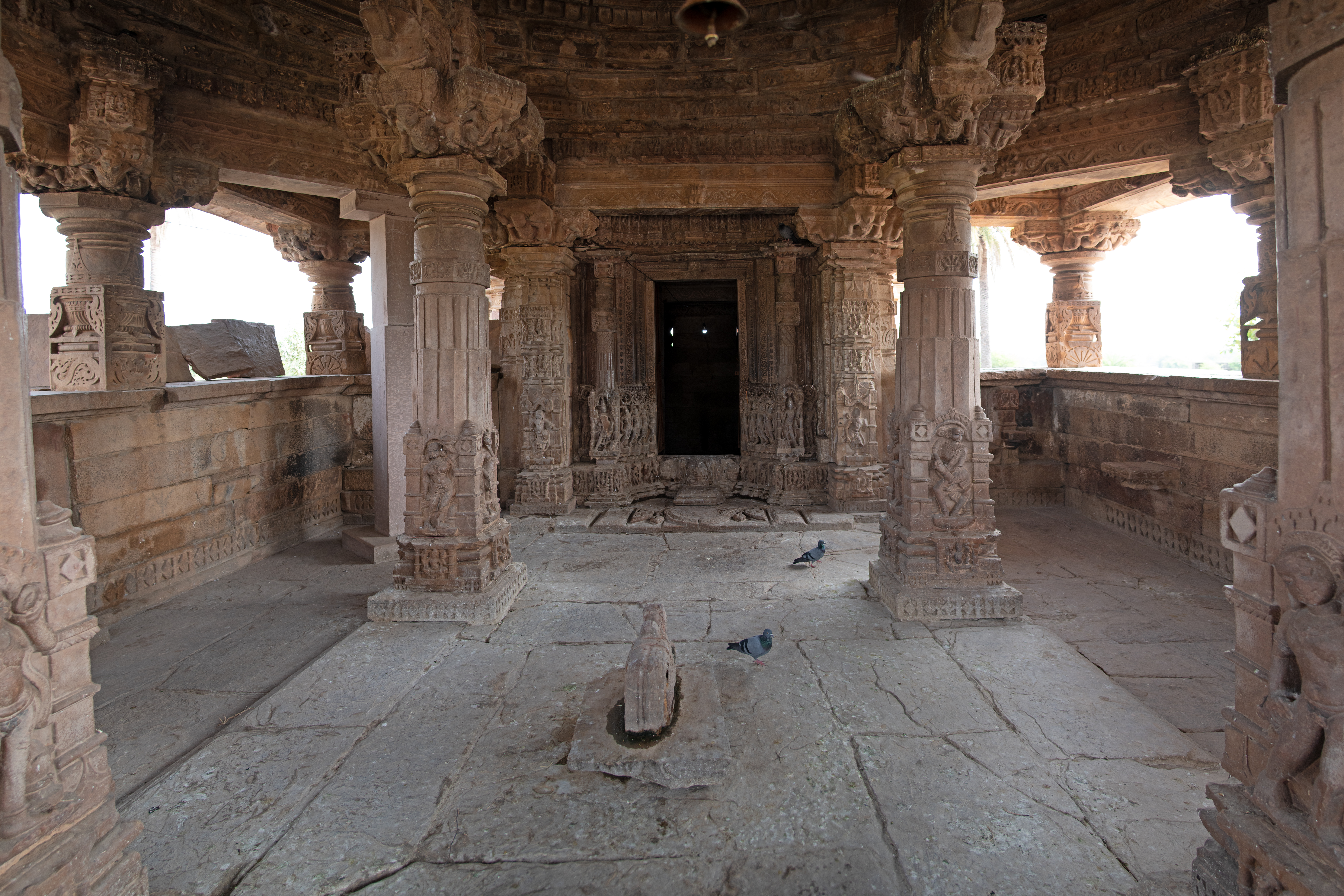 The mukhamandapa (front porch) serves as an entryway to the mandapa (pillared hall) of the Undeshwar Temple, which features lateral extensions. In the mandapa, tall pillars with square bases support an octagonal shaft that transitions into faceted and circular sections. The square bases of the pillars are adorned with carvings depicting various deities, including dikapalas (deities of cardinal directions), surasundaris (celestial damsels), female dancers, and musicians. There is a square shallow platform at the centre on which a Nandi is placed.