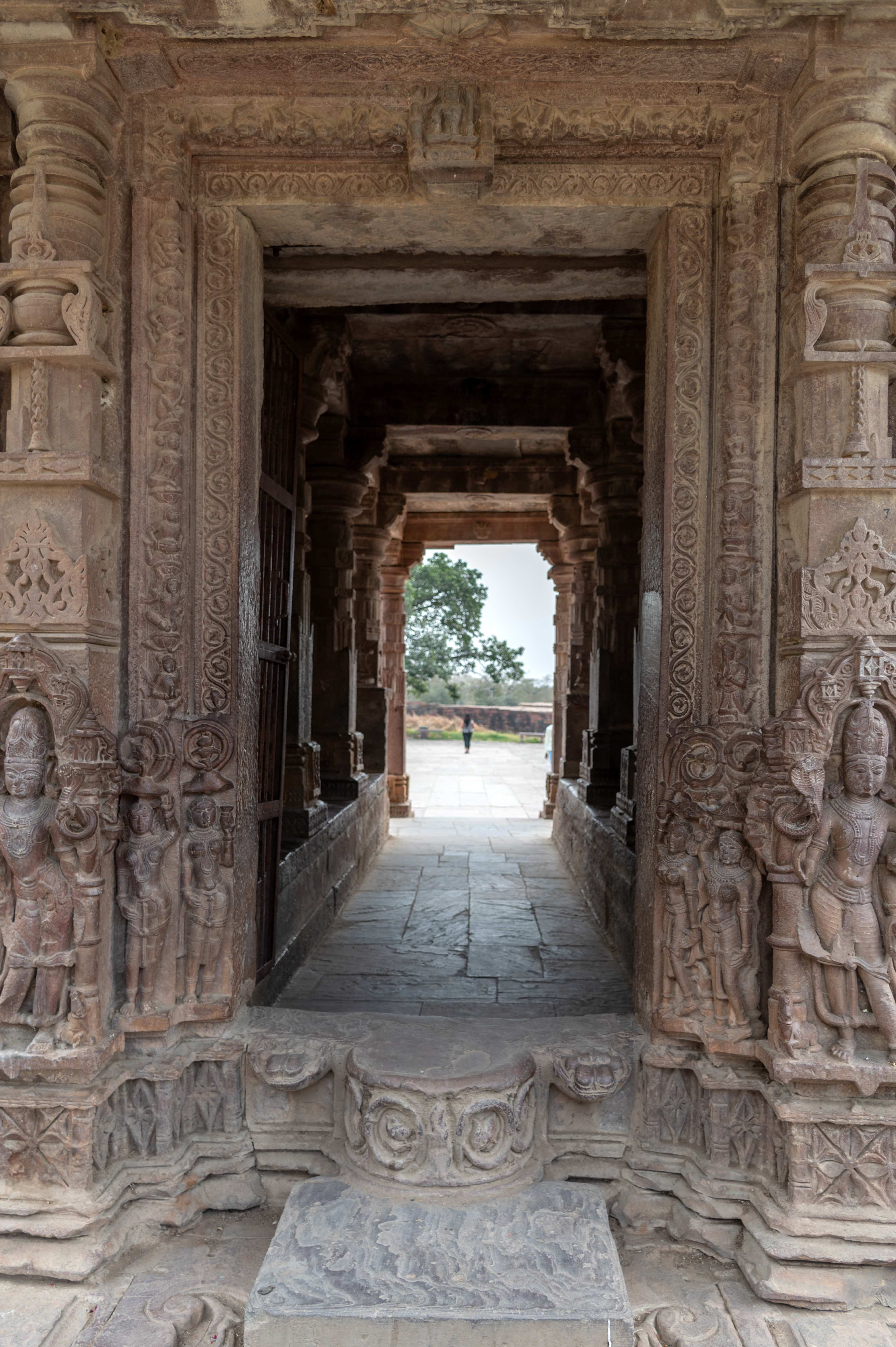 A visitor may enter the gateway's elaborate doorframe/architrave (pratoli). It has intricate designs on the shakkhas (vertical bands), a sculpture at the bottom, and an image of a seated Lakuslisa in the center of the latatabimba (lintel). The Lakuslisa figure is holding a club in hand. On both sides of the doorframe, there are depictions of Shaiva dvarapalas (door guardians).