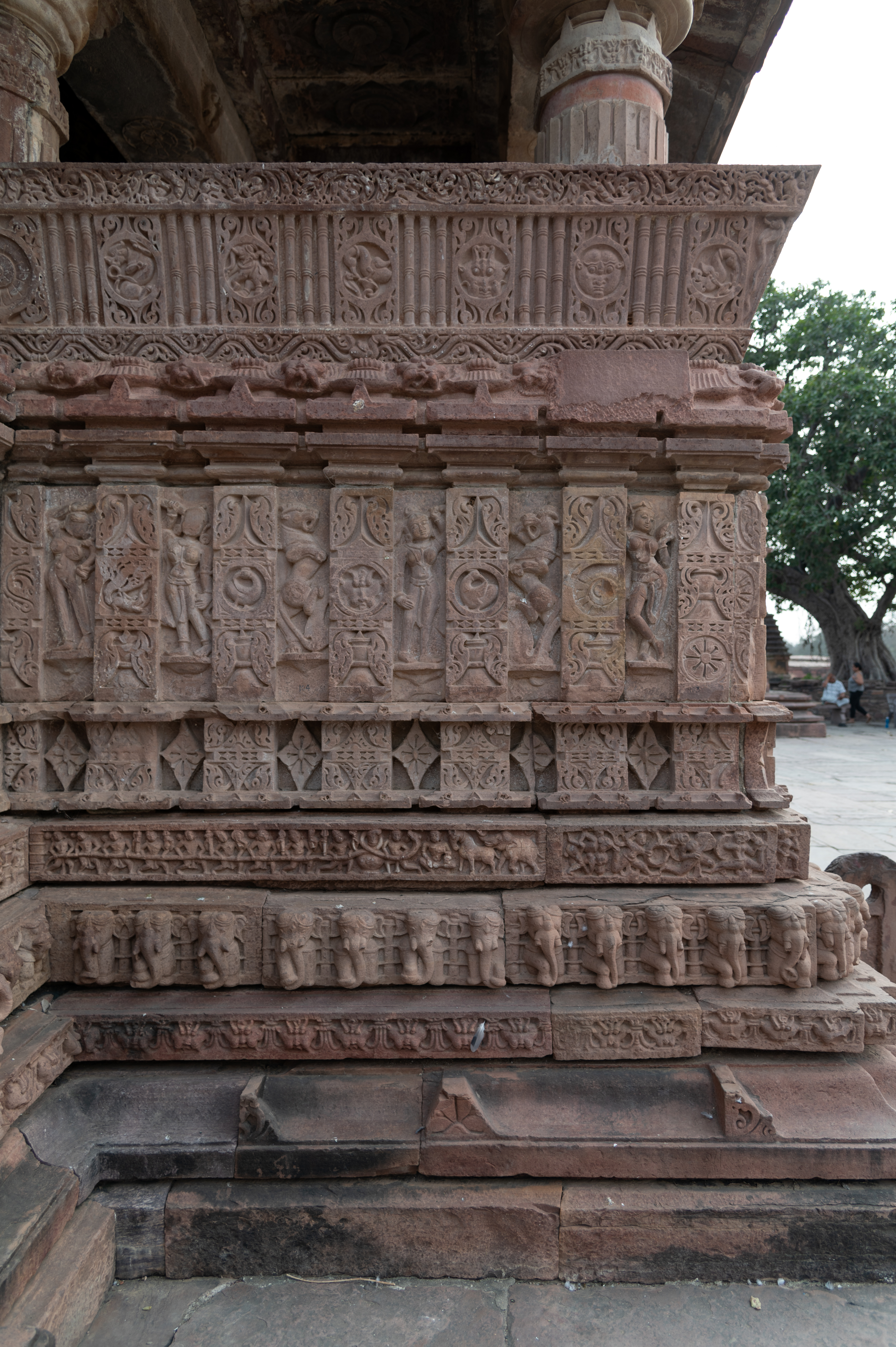 The kakshasana (seat backs) follow the plinth moulding bands, such as the gajathara (elephant band) and narathara (human figure moulding). These have vertical walls, called the vedika (railing), consisting of rectangular, slender geometric patterns that are separated by sculptures. Above the vedika is a slender dwarf wall, which acts as the resting backrest from the inside. These slender walls feature pilaster motifs on the exterior, interspersed with figures framed by circular niches. The kakshasana serves as the base of the temple's semi-open mandapa (pillared hall).