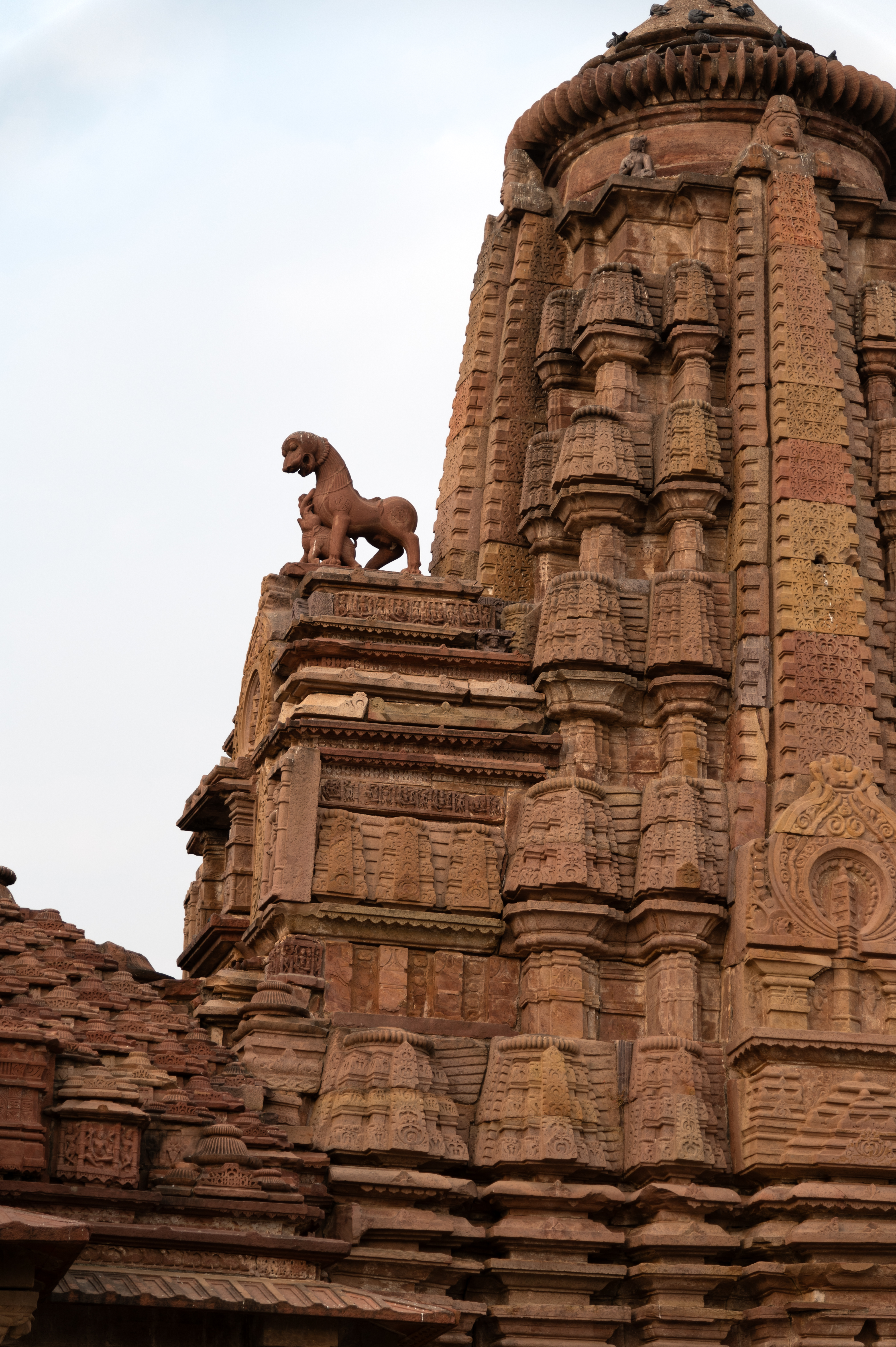 This is the south-facing elevation of the Mahanaleshwar Temple's shikhara (superstructure). The front side of the shikhara has an elaborate shukanasa (an ornamented projection over the entrance of the sanctum), with a lion sculpture on top. The shukanasa has a niche at its centre, and above it is a chaitya (horseshoe-shaped) medallion. The shukanasa mouldings are similar to the temple's plinth mouldings. The three bhumija aedicules on each side of the shikhara are a notable feature.