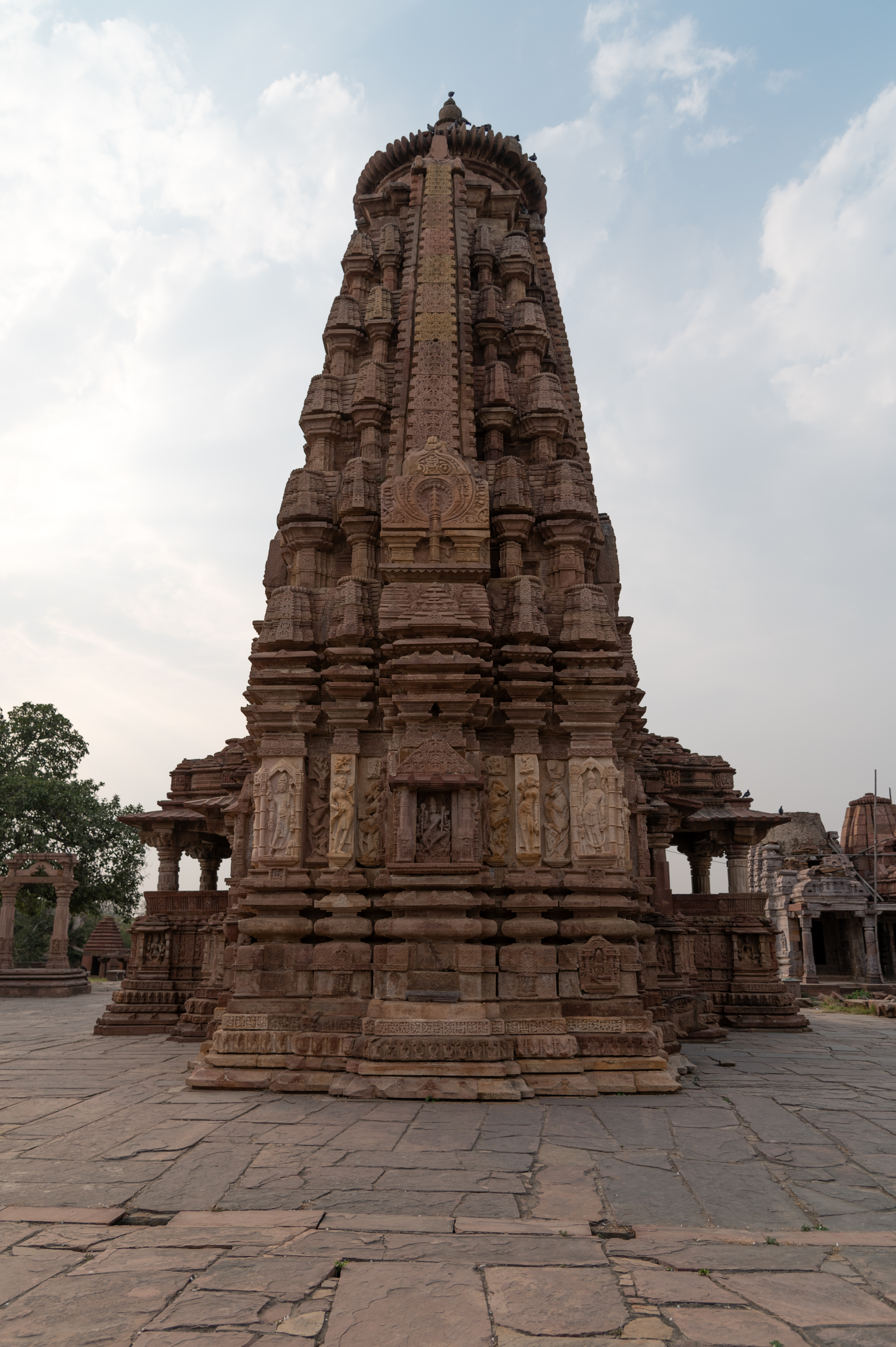 This is the rear or east-facing elevation of the Mahanaleshwar Temple, reflecting the bhumija temple shikhara (superstructure). All four sides of the shikhara have cardinal bands, called lata, at the centre. Rows of miniature shikharas, or bhumis, fill the four quadrants that form in between these. These motifs depict the details of the main shikhara. The lata's base has an ornamental window and a chaitya dormer with a miniature kutastambha motif.