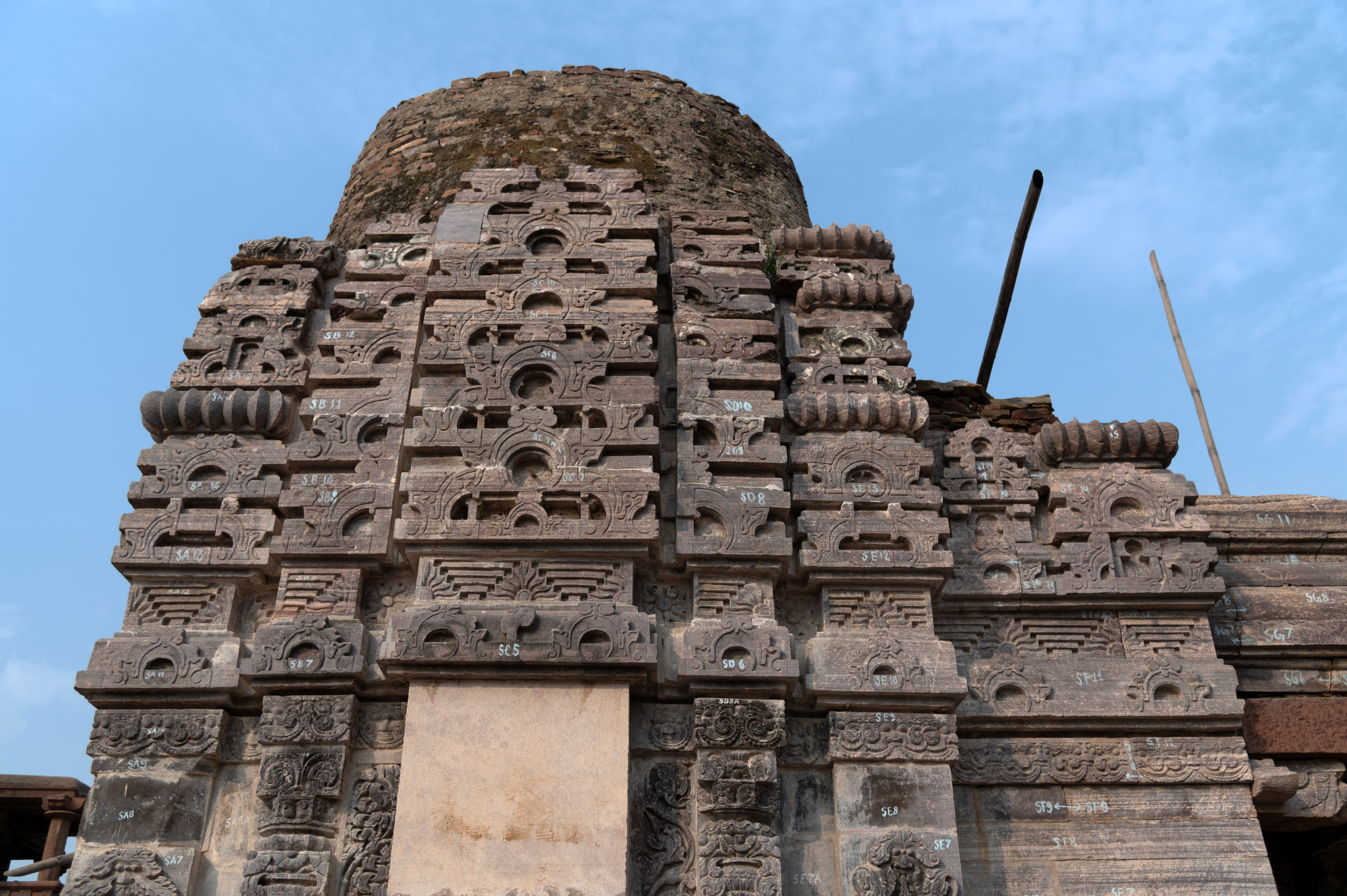 The latina shikhara (monospire superstructure) of the side shrine of the Triple-shrine Temple still has two bhumi khandas (tiers) on its south-facing elevation. Combinations of gavaksha (dormer window) designs compose all the latas (bands) of the shikhara. The east-facing side of the temple has a protruding shukanasa (projection over the entrance of the sanctum), which is connected to the main shikhara and acts as the superstructure of the mandapa (pillared hall) of the temple. The corner bands of a latina shikhara are called venukosha. Tiers of diminishing sizes comprise this structure. Each of these tiers is separated by a flat, ribbed disc known as the amalaka.