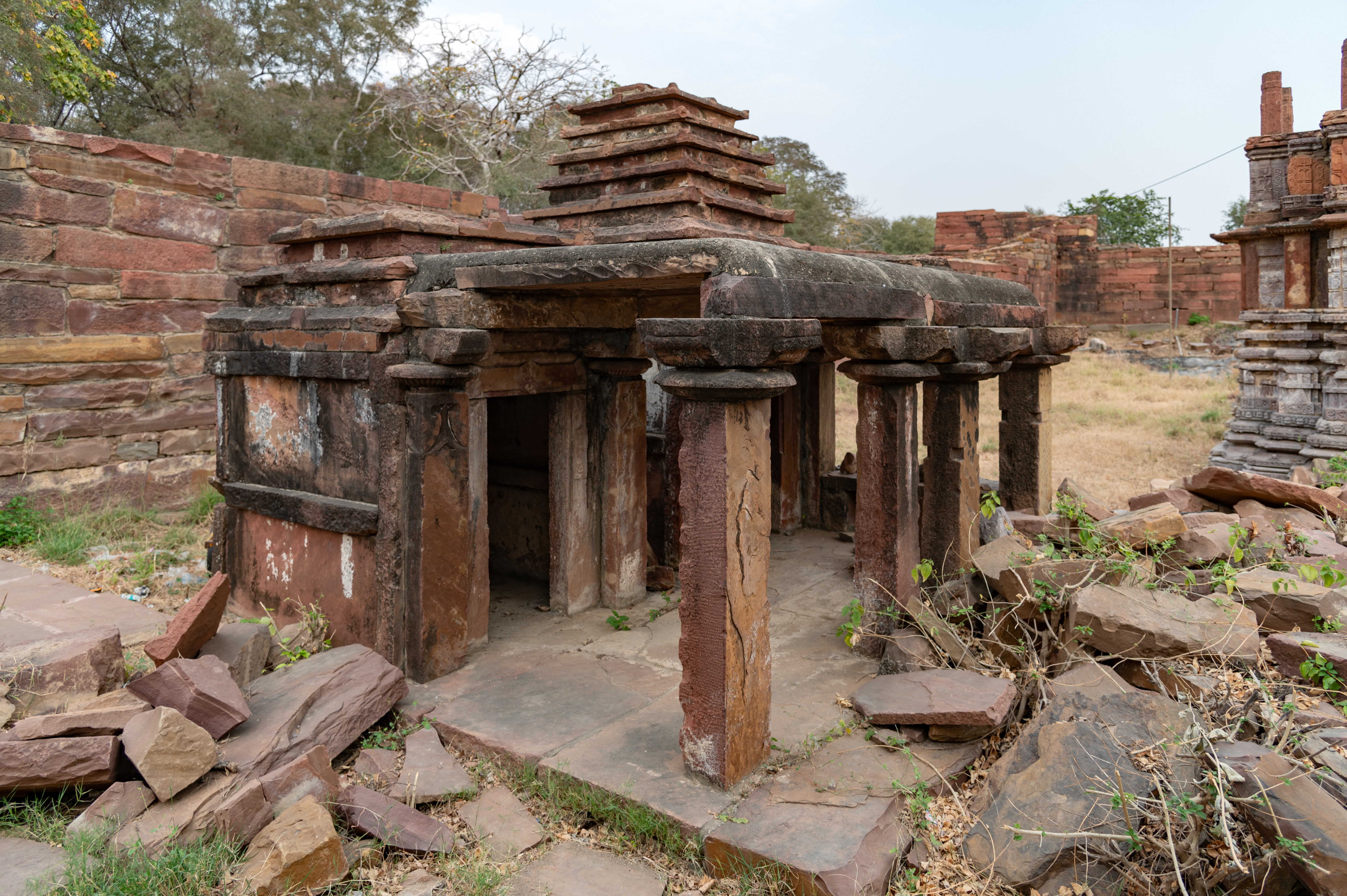 Similar to the western boundary of the Mahanaleshvar temple complex, the northern side also has two temples that stand close to the main temple. A ruinous shrine is visible here, devoid of ornamentation. Its superstructure has not survived. A colonnade fronts a row of small cells that make up its superstructure. The colonnade's pillars have plain shafts.
