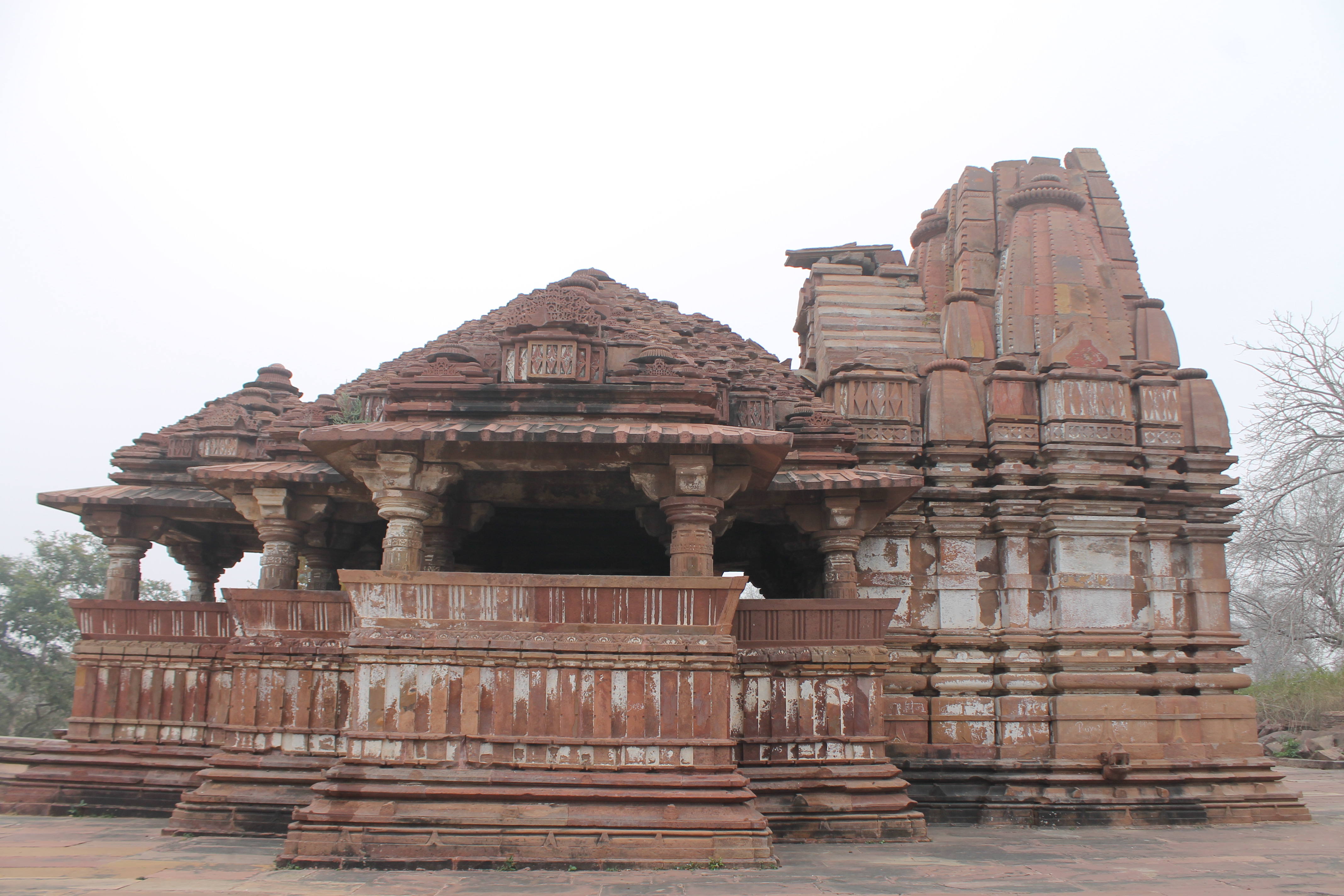 Image 4: The north-facing elevation of the Suhaveshwar Temple is identical to the south-facing side. The protruding shukanasa, frontal of the shikhara (superstructure), is visible here. It is a semi-circular opening. The topmost portion of the main shikhara is missing. Along the elevation of the temple, the mandapa (pillared hall) shikhara has a row of large ghantikas (aedicules) that cascade from the centre. The base of the mandapa shikhara has a square block with diamond motifs that is topped by a gavaksha (dormer window) design.