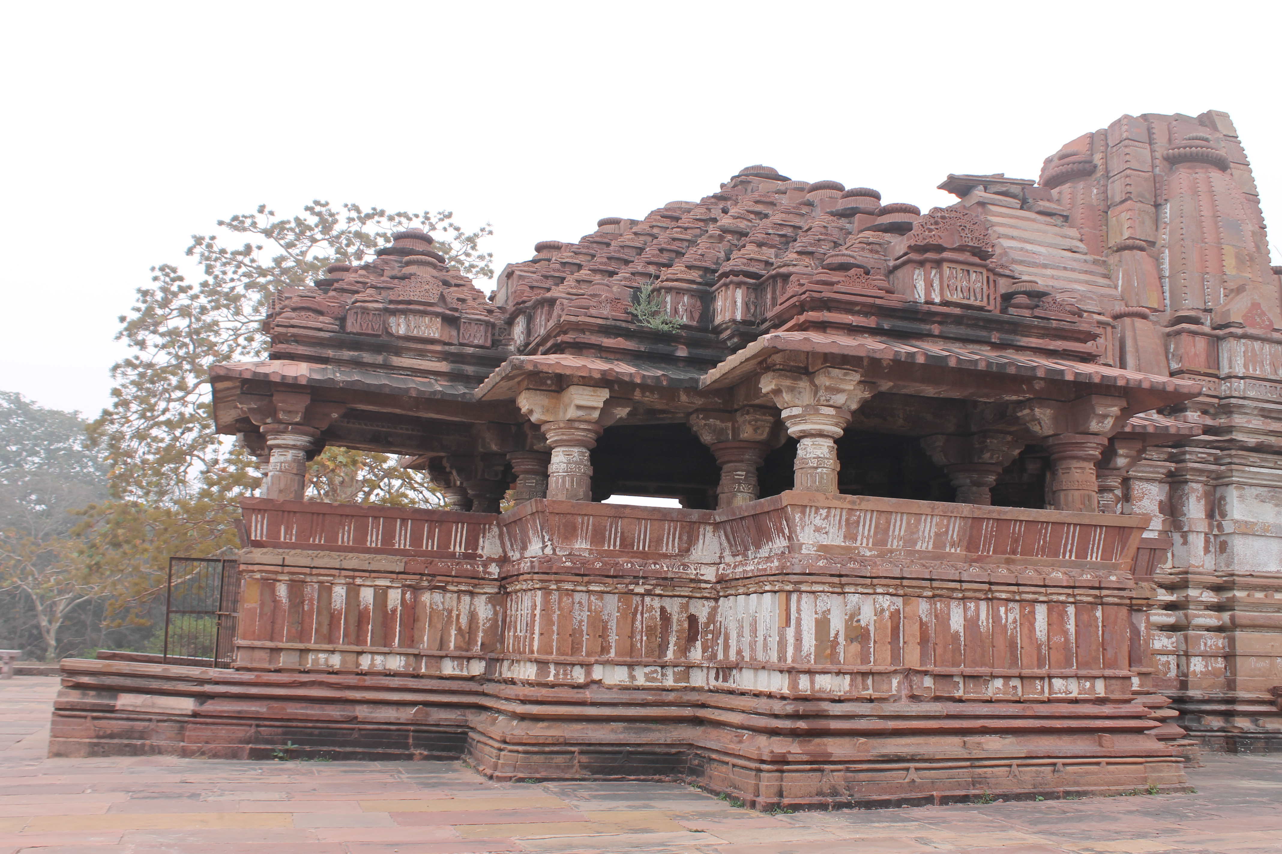 This is a view of the south elevation of the Suhaveshwar Temple's mandapa (pillared hall). The mandapa has two lateral transepts on the north and south sides. Both the mukhamandapa (front porch) and the mandapa have pyramidical shikharas atop them. The shikhara (superstructure) on the mandapa is of the samvarana (pyramid-shaped) variety. The juncture of the pillars of the mandapa and the shikhara are marked by a protruding chajja (balcony).