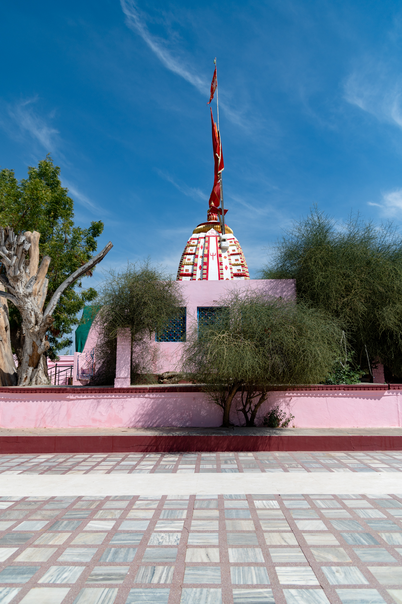 Image 1:  View from the rear side, west-facing, of the Suswani Mata Temple consisting of the newly added walls surrounding it along with the Kera tree to the south and other trees that are considered sacred by devotees. The original Latina shikhara (mono-spired north Indian variety of temple superstructure) can also be seen.