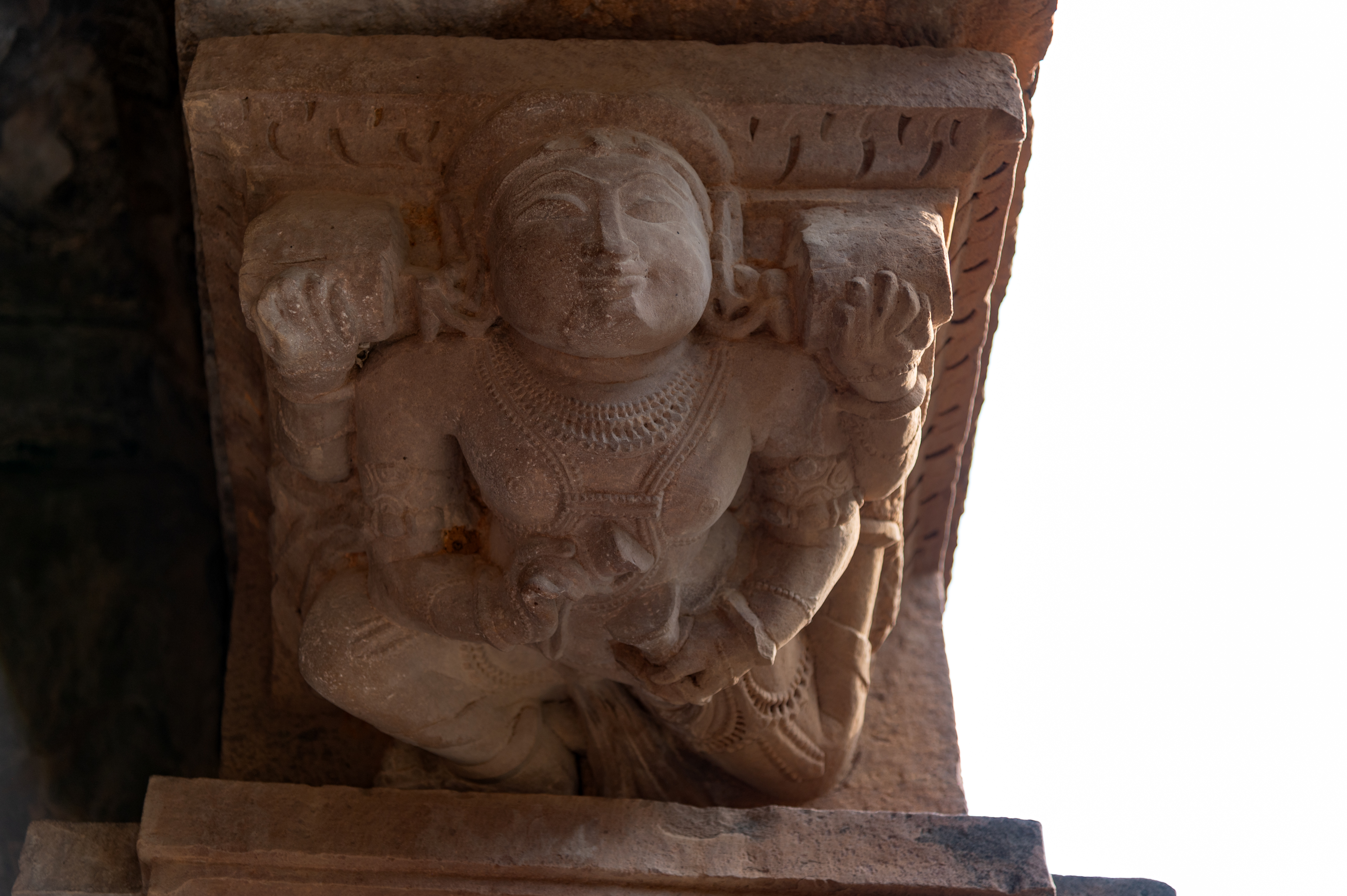  A four-armed bharavahaka (load bearer) is depicted on the left pilaster of the antarala (vestibule or antechamber) of the Kaner-ki-Putli Temple. It is shown bearing the weight of the roof with its upper hands while using its lower hands to play the cymbals.