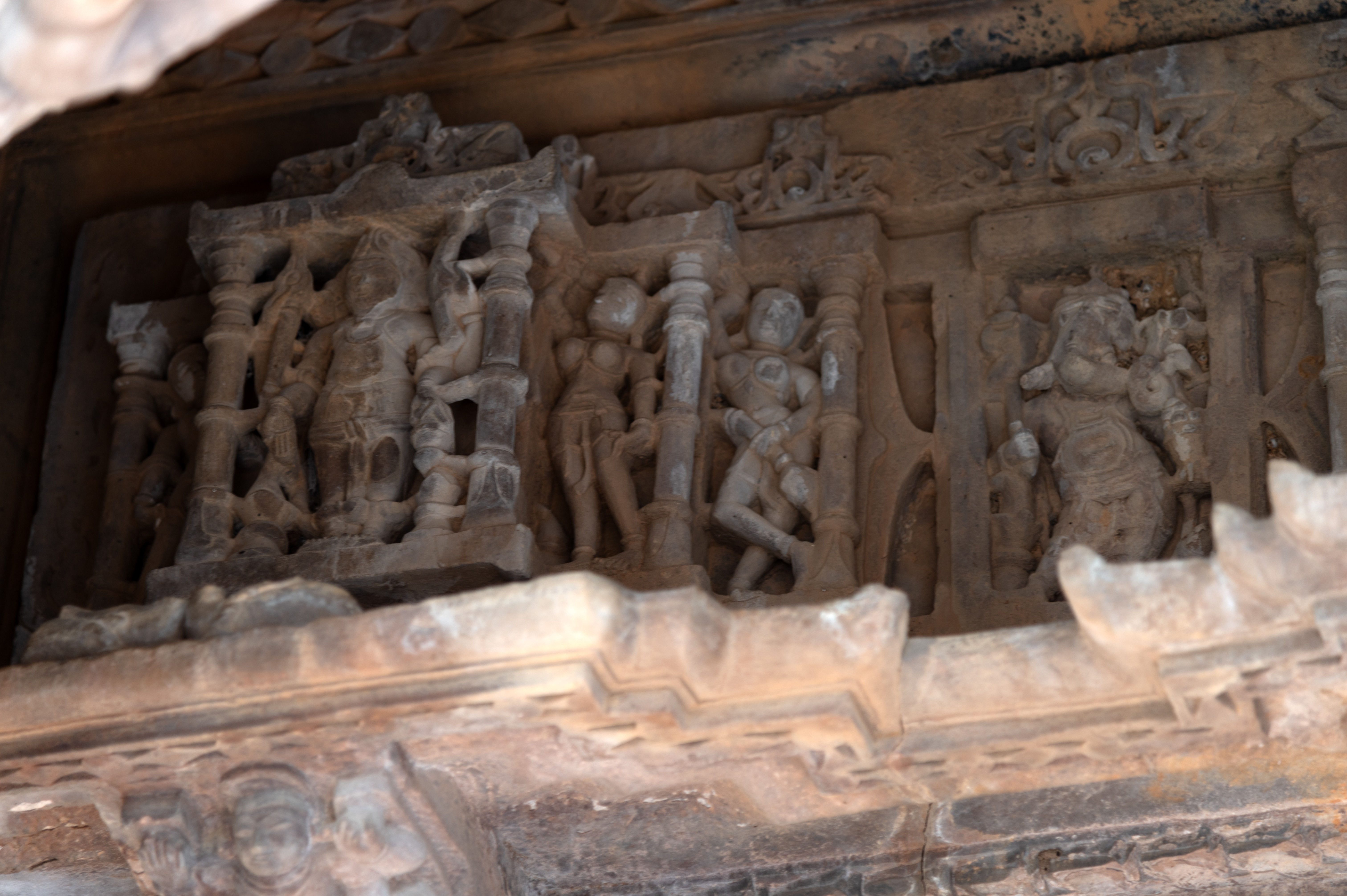 On the left of the uttaranga (entablature) above the lintel of the garbhagriha (sanctum sanctorum), Brahma is depicted with three faces and four arms. His upper hands carry a shruka (a sacrificial spoon) and a pustaka (manuscript), while his lower hands hold a kamandalu (water carrier or pot) and display varadaksha (a hand held in the boon-giving gesture, with a rosary in it).