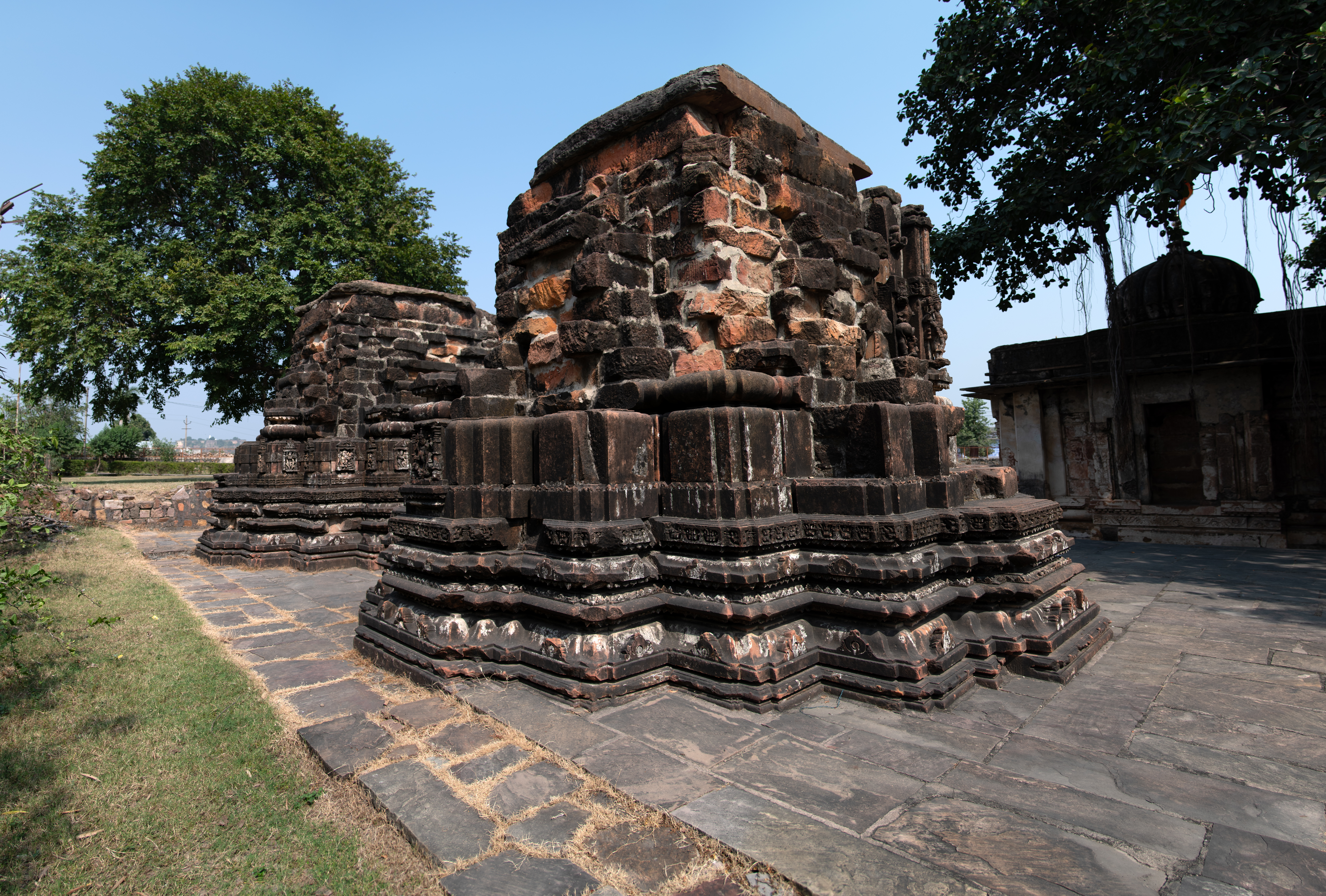 The rear view (northwest) of the Vishnu and Shiva temples behind the Sitaleshwar Temple shows that the temples are in disrepair. Both temples retain their ornately carved base mouldings, but their jangha (wall) and shikhara (superstructure) suffer severe damage.