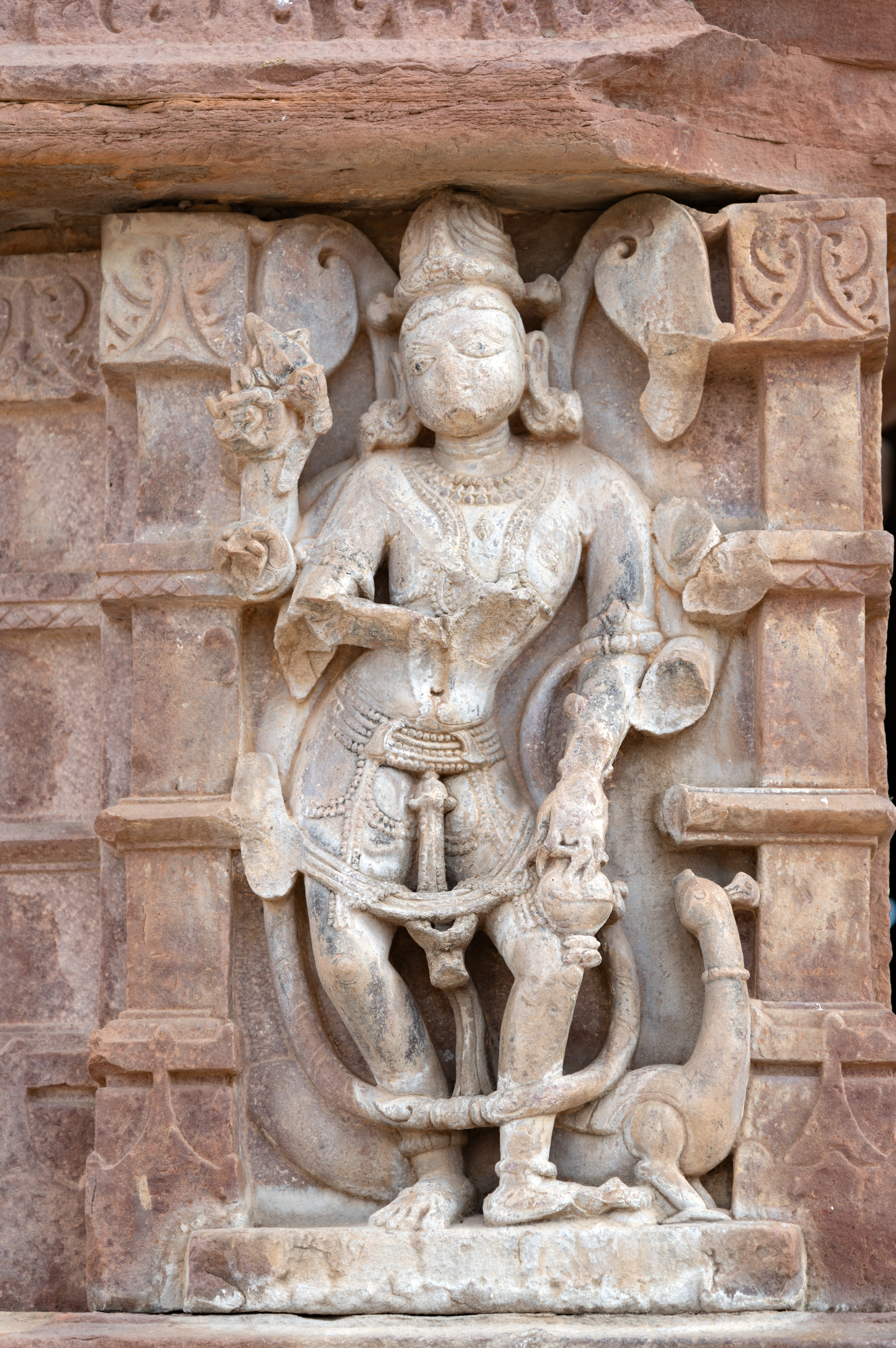 Kartikeya is depicted on the external walls of the mandapa (pillared hall). Though most of his arms are fragmented, he holds a kamandalu (water pot) in his intact hand, symbolizing purity and divinity. He is identifiable by his vahana (mount), the mayura (peacock), depicted below him.