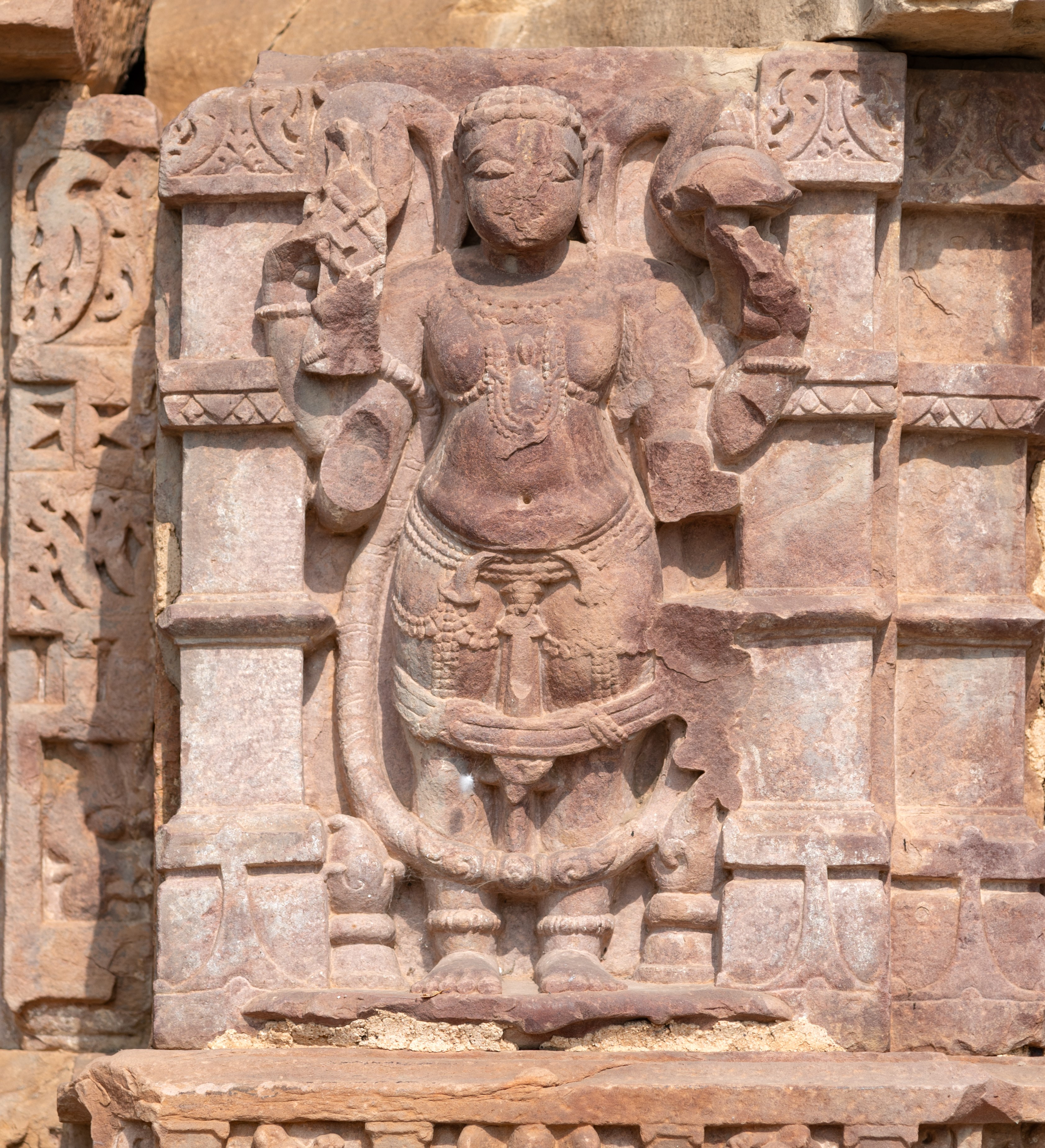 On the kakshasana (seat backs), the depiction of Vamana, an avatar of Vishnu, stands prominently. Vamana is portrayed with four arms, although two are damaged. In his upper right hand, he holds a pustaka (book). This attribute holds significant symbolism, as Vishnu in his Vamana avatar assumes the form of a Brahmin, embodying the essence of divine wisdom contained within the Vedas.