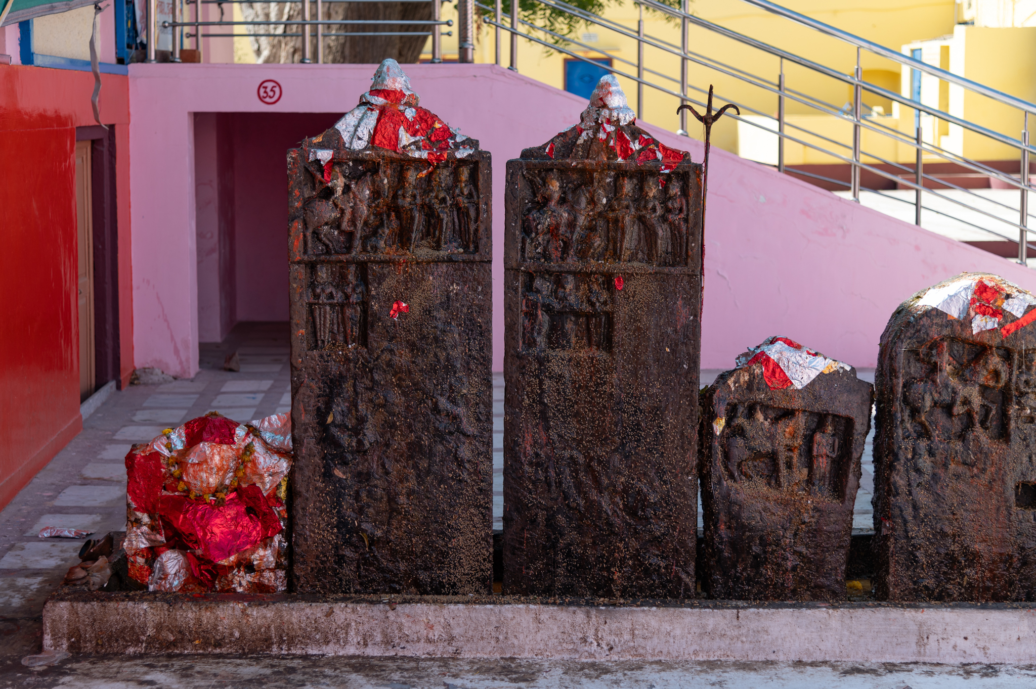 Seen here are two of the largest hero stones found among the fragments in the Suswani Mata Temple. Interestingly, both slabs feature a similar type of depiction where the upper half shows certain human figures while the lower half of the stone slab is empty. The finials of the hero stones are stylized as temple shikharas (superstructures), specifically latina shikharas (mono-spired). Approximately four feet in height and a half foot in width, these hero stones are unique specimens and constitute an important corpus of historical data. The plain portions of the stone slabs have very faint remains of inscriptions, which might contain information about the person in whose honour the hero stone was carved.
