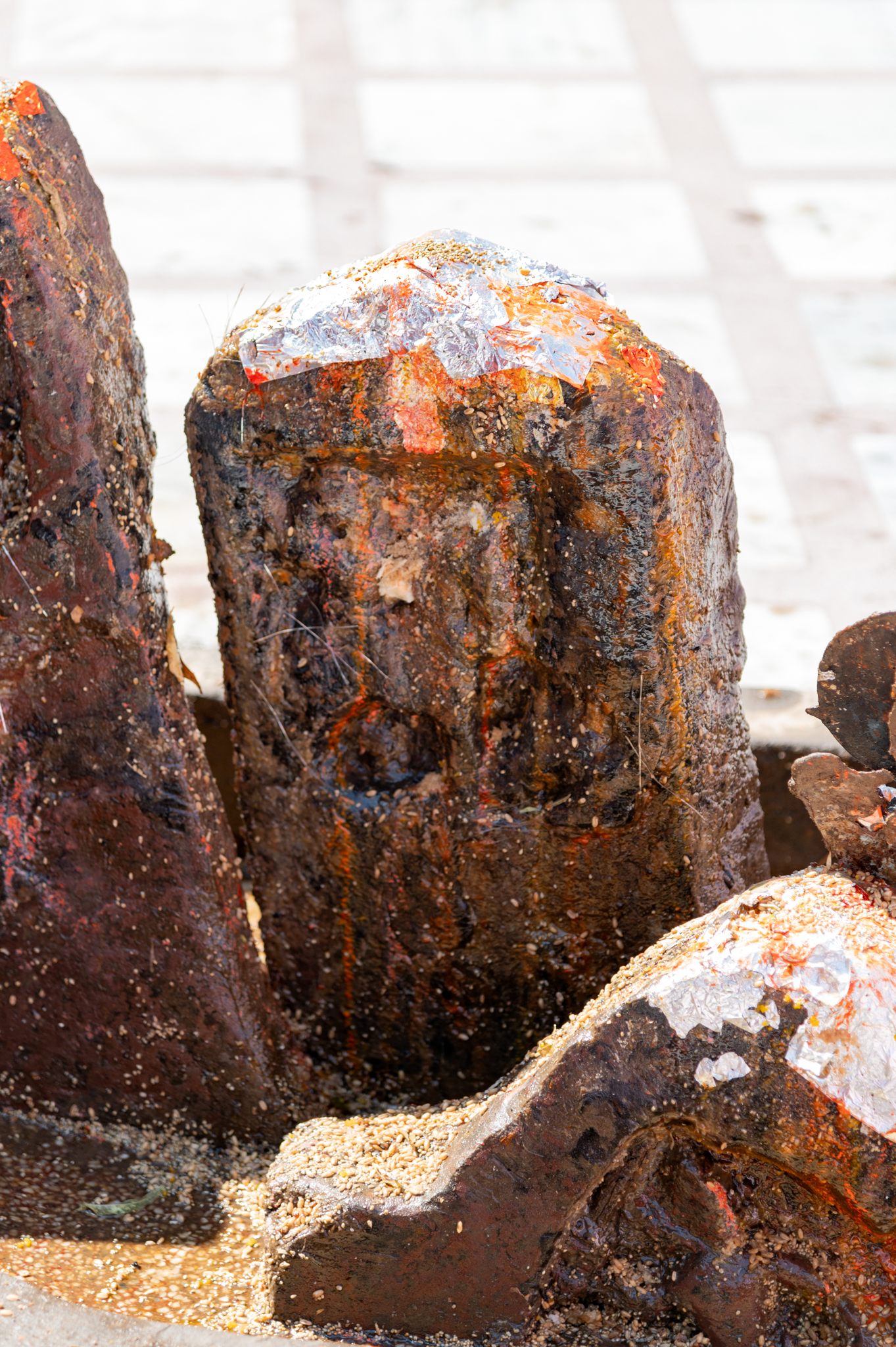 Seen here is one of the most damaged hero stone fragments found within the Suswani Mata Temple Complex. Carved on a rectangular slab with a triangular top, this fragment features figures carved inside a relief niche. Although not clearly visible, the carving depicts the hero riding on a horse. The presence of inscriptions on the lower portion of the hero stone is uncertain due to its condition. However, given its stylistic similarity to adjacent fragments, it is plausible that this fragment originally included some form of inscription.