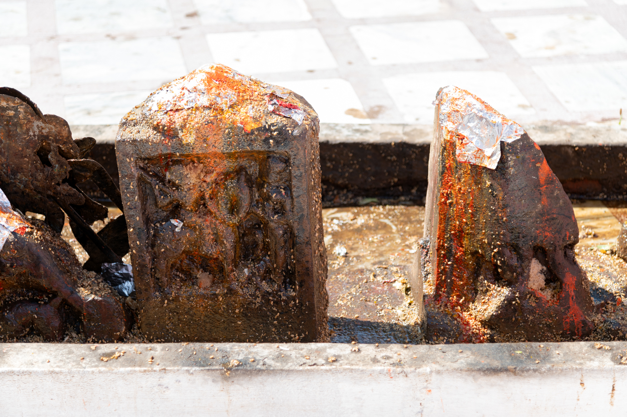 A fragmentary hero stone depicts the hero riding on horseback, wielding a sword and shield, poised for battle against the enemy. Adjacent to him stands a human figure with folded hands, likely another small figure kneels in front of the standing figure, bowing down. The narrative depicted on this hero stone is similar to other hero stones in the complex.