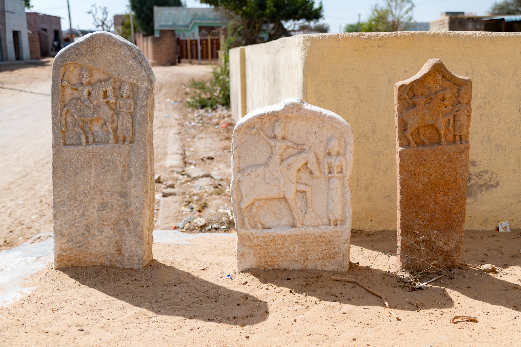 Typically, the front side of the Hero Stones depicts a hero riding on horseback, accompanied by a female figure standing in front of him with her hands folded in namaskar mudra (salutation gesture). The size of this depiction might vary on each stone, but they maintain stylistic similarity. Sometimes, these figures include inscriptions that provide details such as the person honoured by the hero stones and the date of its creation. The dates from legible inscriptions on the Hero stones are from 1500 VS onwards, placing them in the 15th-16th centuries CE.